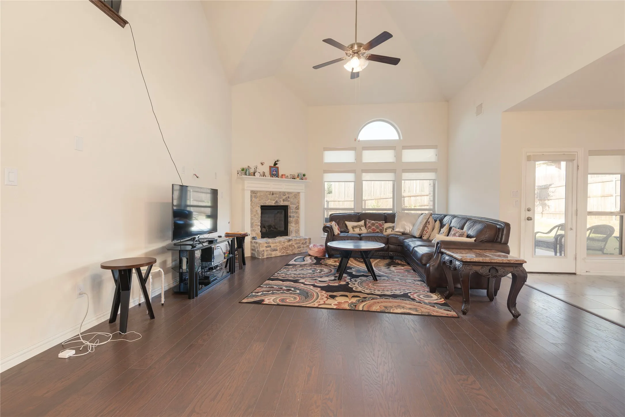 Spacious living area featuring high vaulted ceilings, dark wood-finish flooring, and a stone-faced fireplace with a mantel