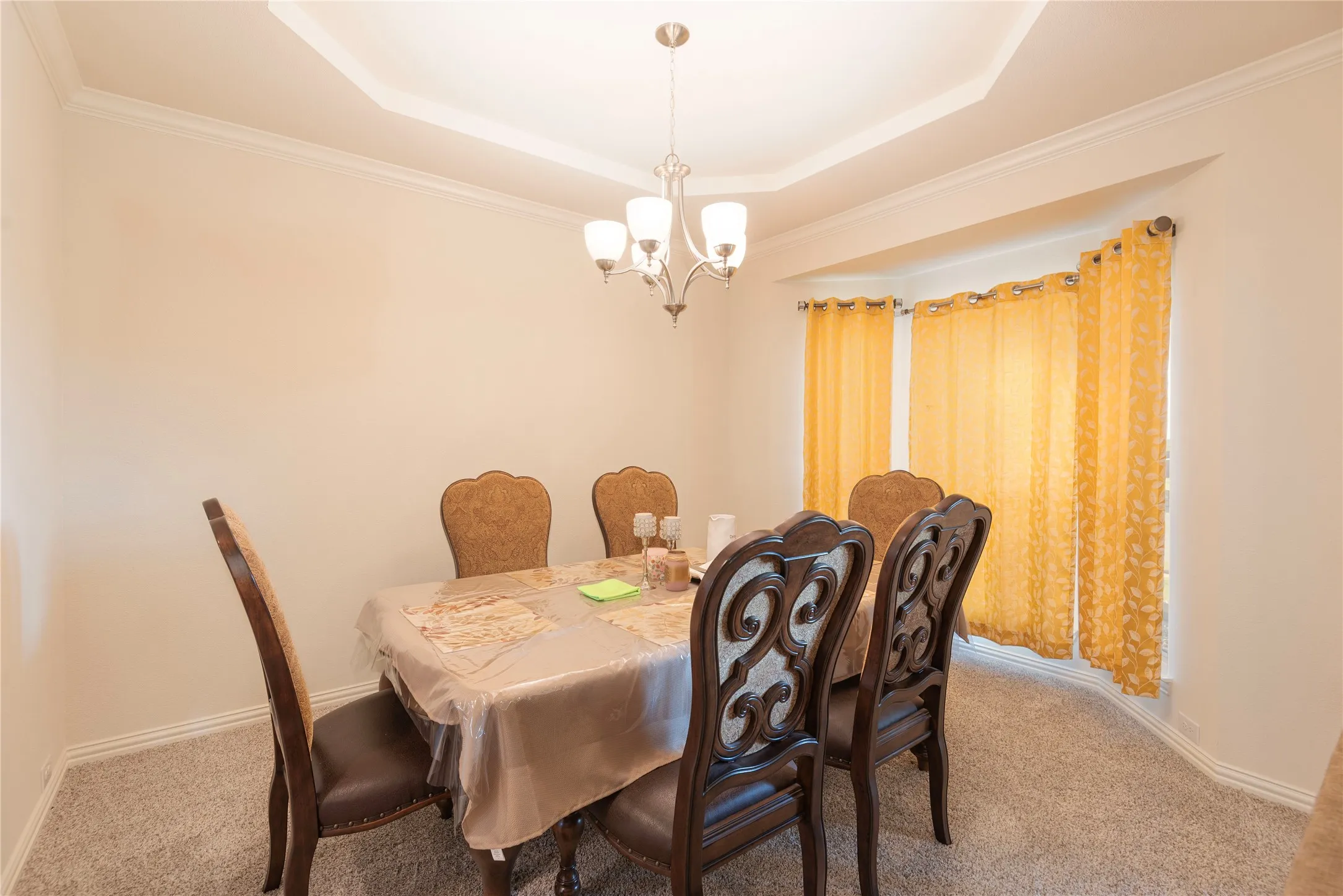 Dining area featuring a tray ceiling with crown molding, a central chandelier, and a bay window