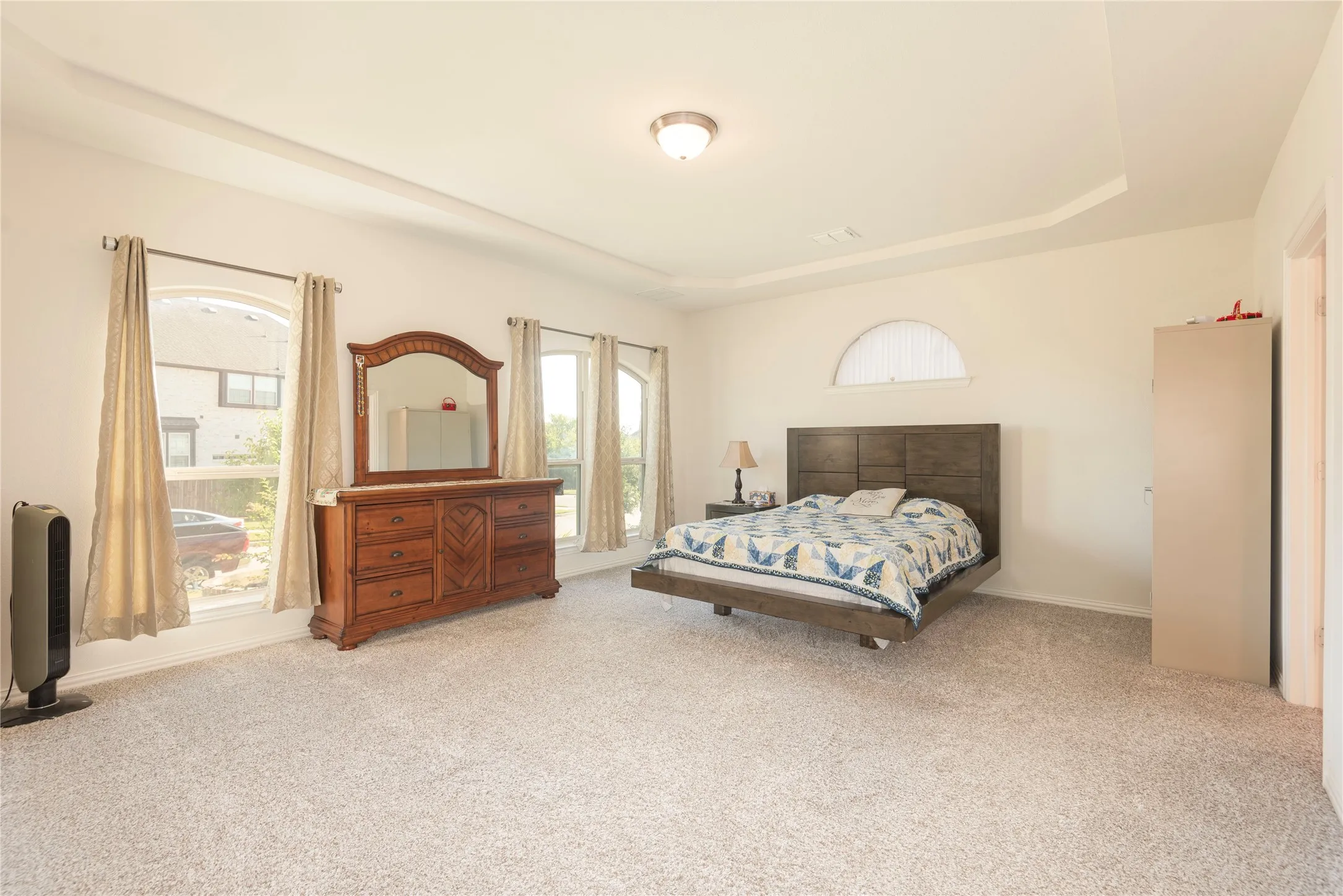 Spacious room featuring light-toned carpet flooring, a tray ceiling, and white wall finishes