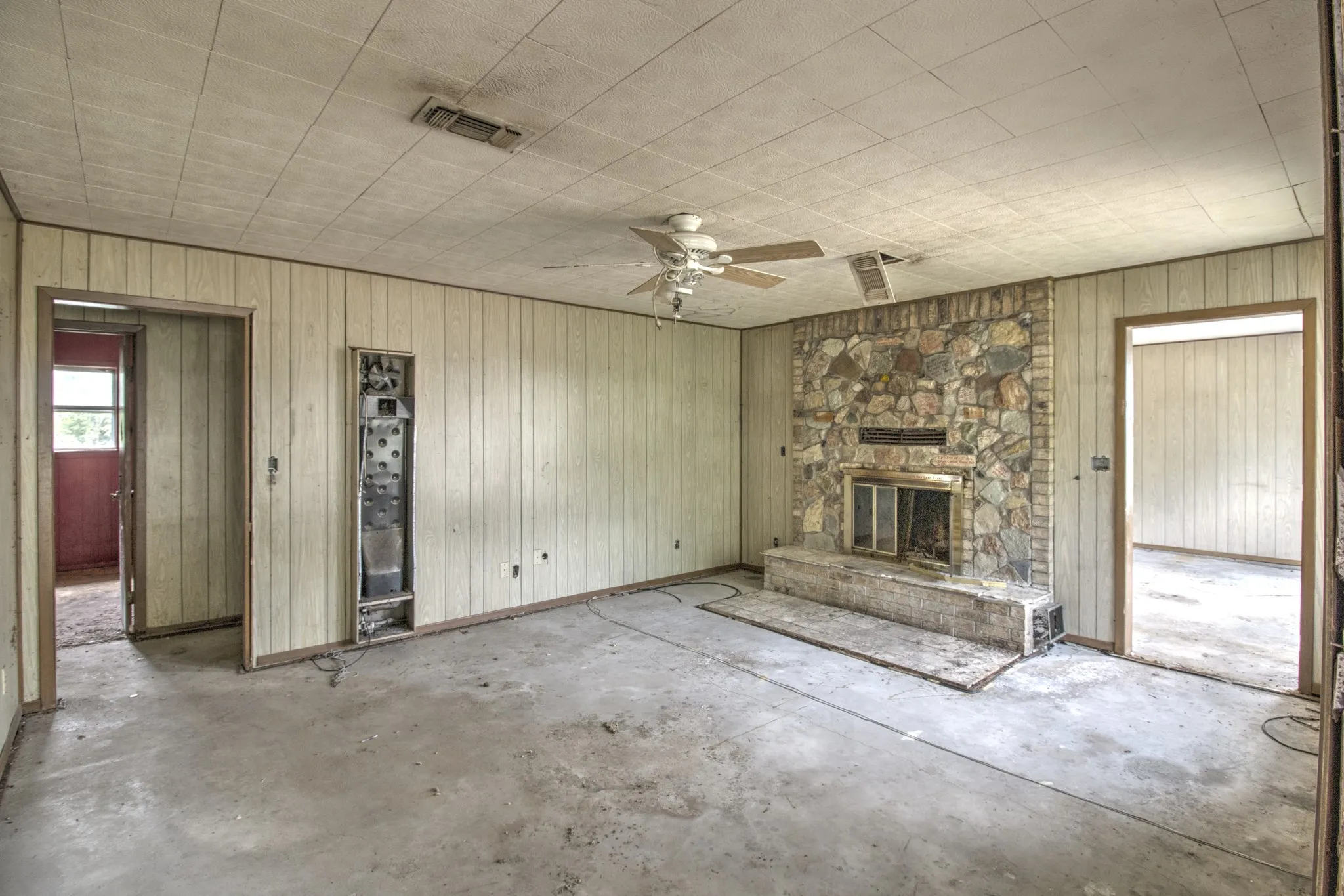 Spacious room featuring a prominent stone fireplace with a raised hearth, light-toned vertical wall paneling, and a ceiling fan