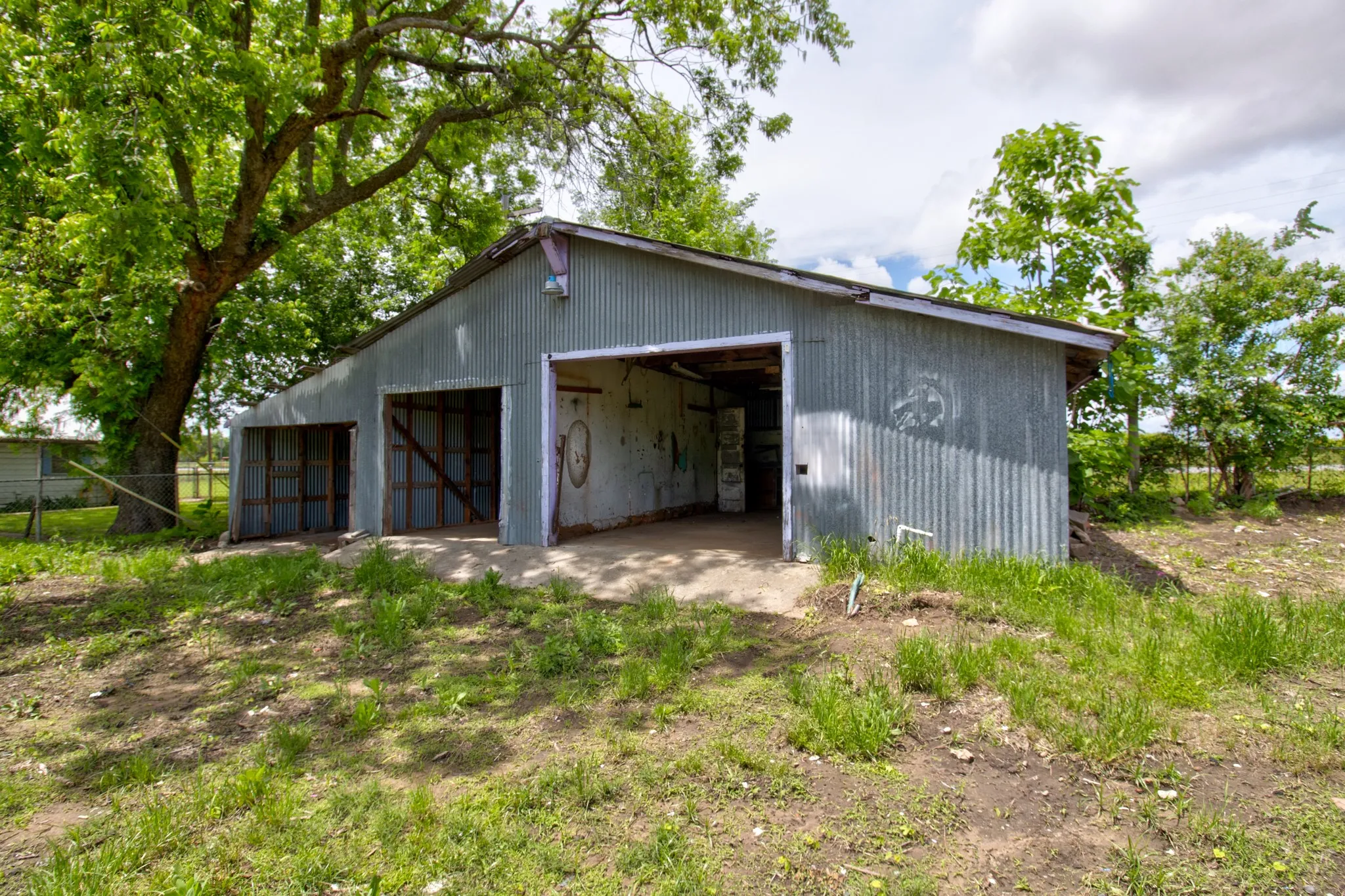 Corrugated metal outbuilding with two bays, featuring a sloped roofline and a concrete pad