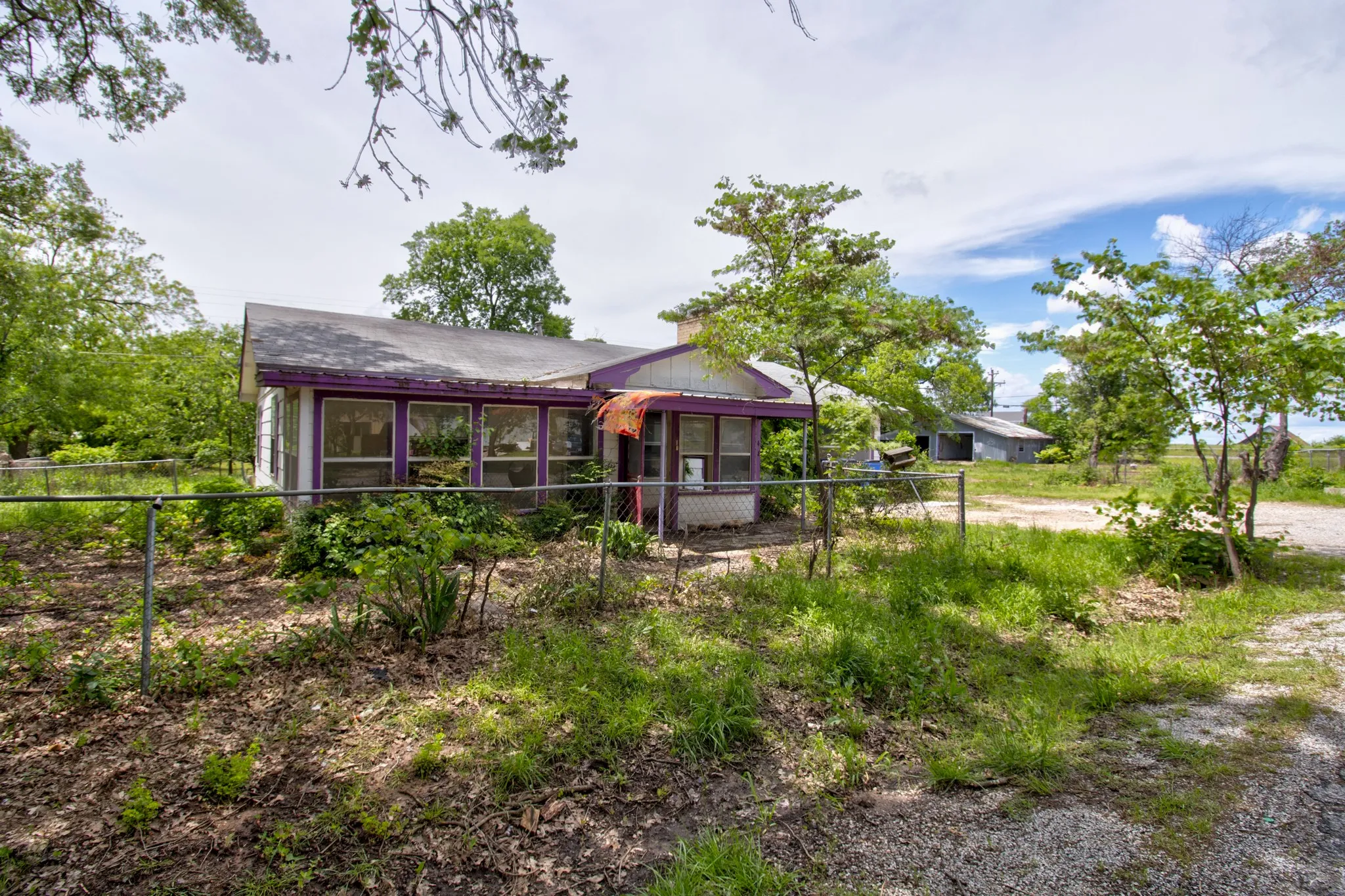 Single-story residence featuring a chain-link fence, mature trees, and a sunroom with multiple windows
