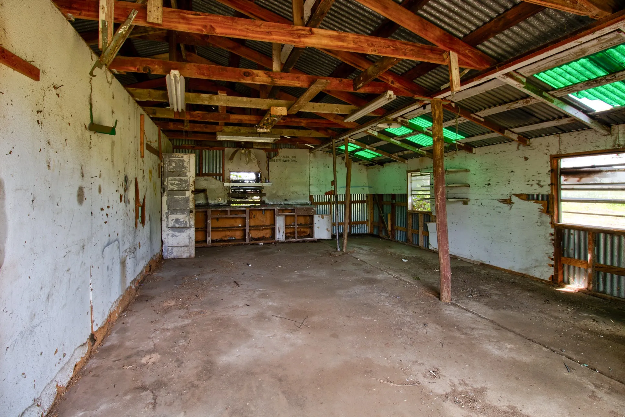 Spacious interior featuring exposed wood beams, corrugated metal roofing, and multiple window openings