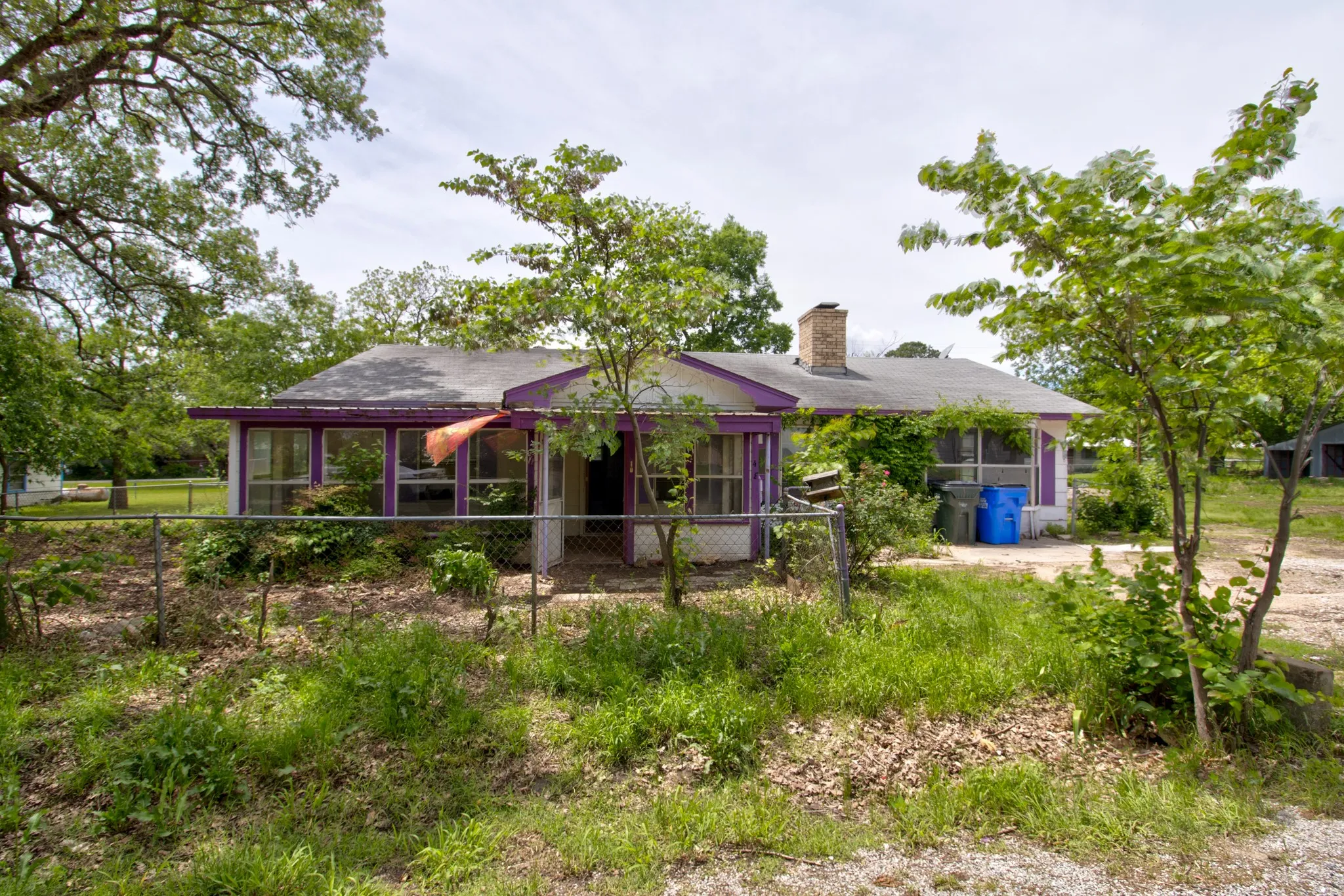 Single-story residential structure featuring a screened porch entry, brick chimney, and mature trees