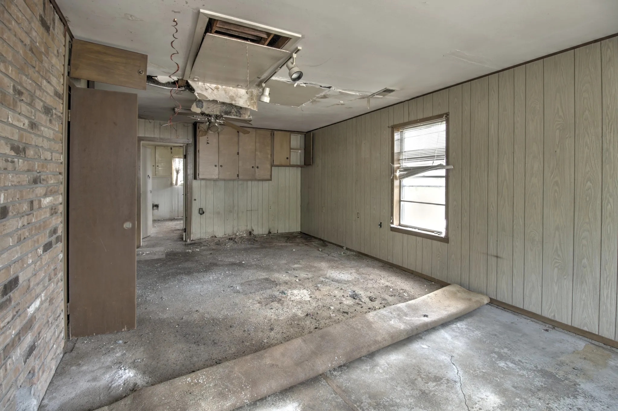 Interior space featuring brick wall accents, wood paneling, a window with blinds, and built-in cabinetry