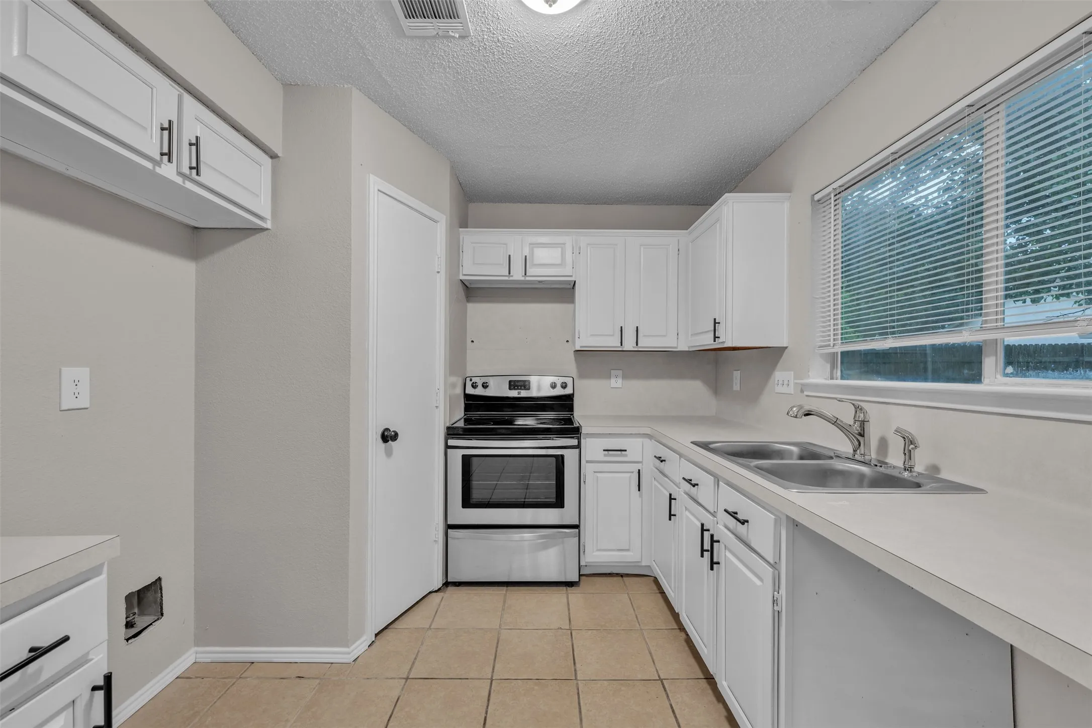 Kitchen featuring white cabinetry with black hardware, light-toned countertops, and tile flooring