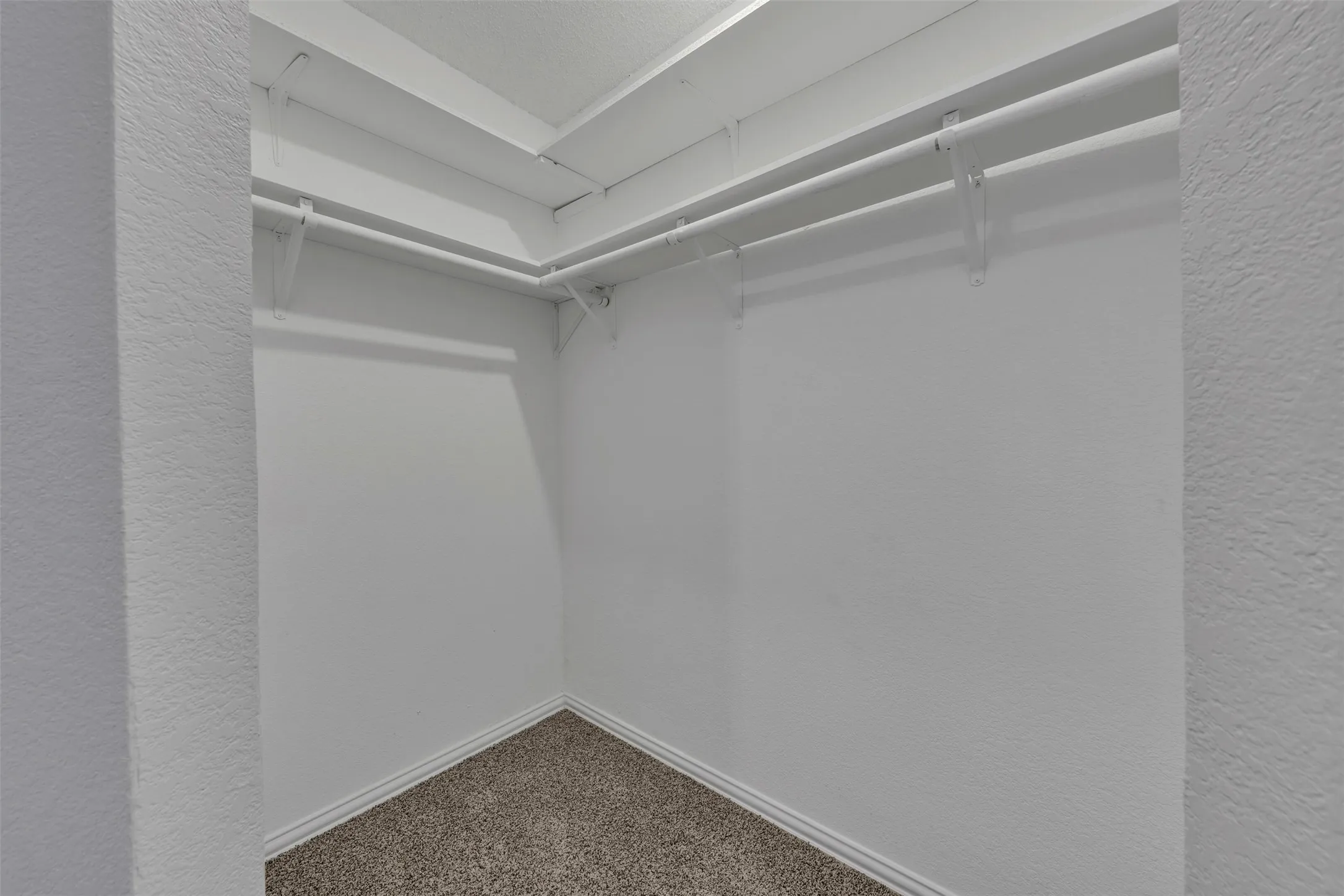 Walk-in closet with carpet flooring, white baseboards, textured walls, and integrated shelving with hanging rods