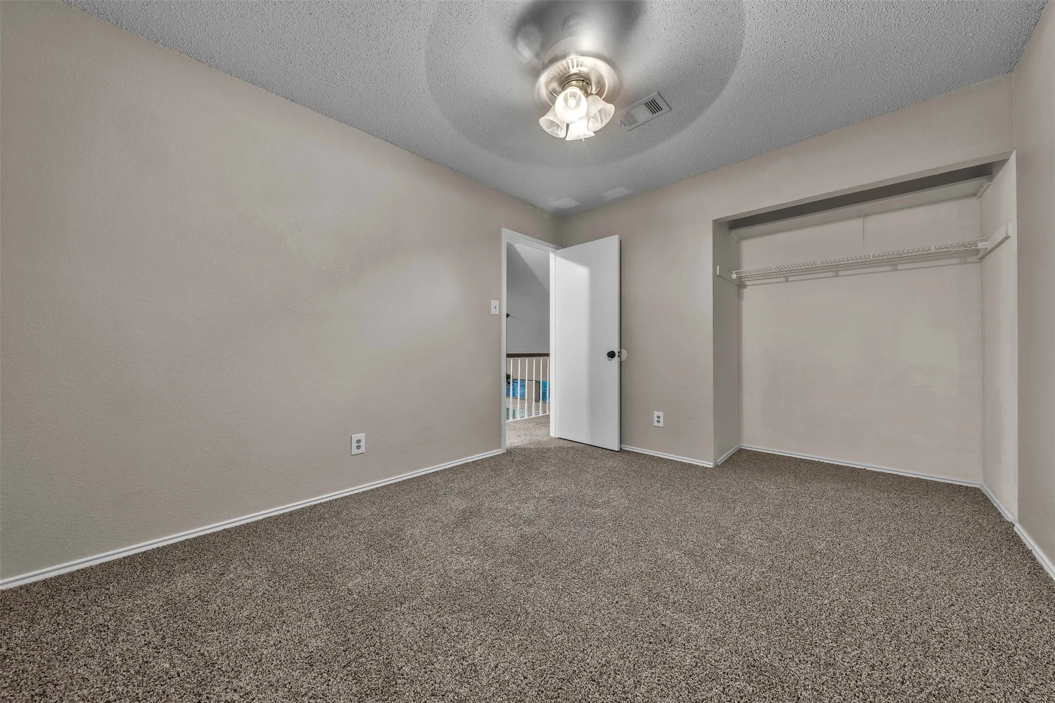 Carpeted room featuring a neutral wall color, overhead ceiling light fixture, and an open closet with wire shelving