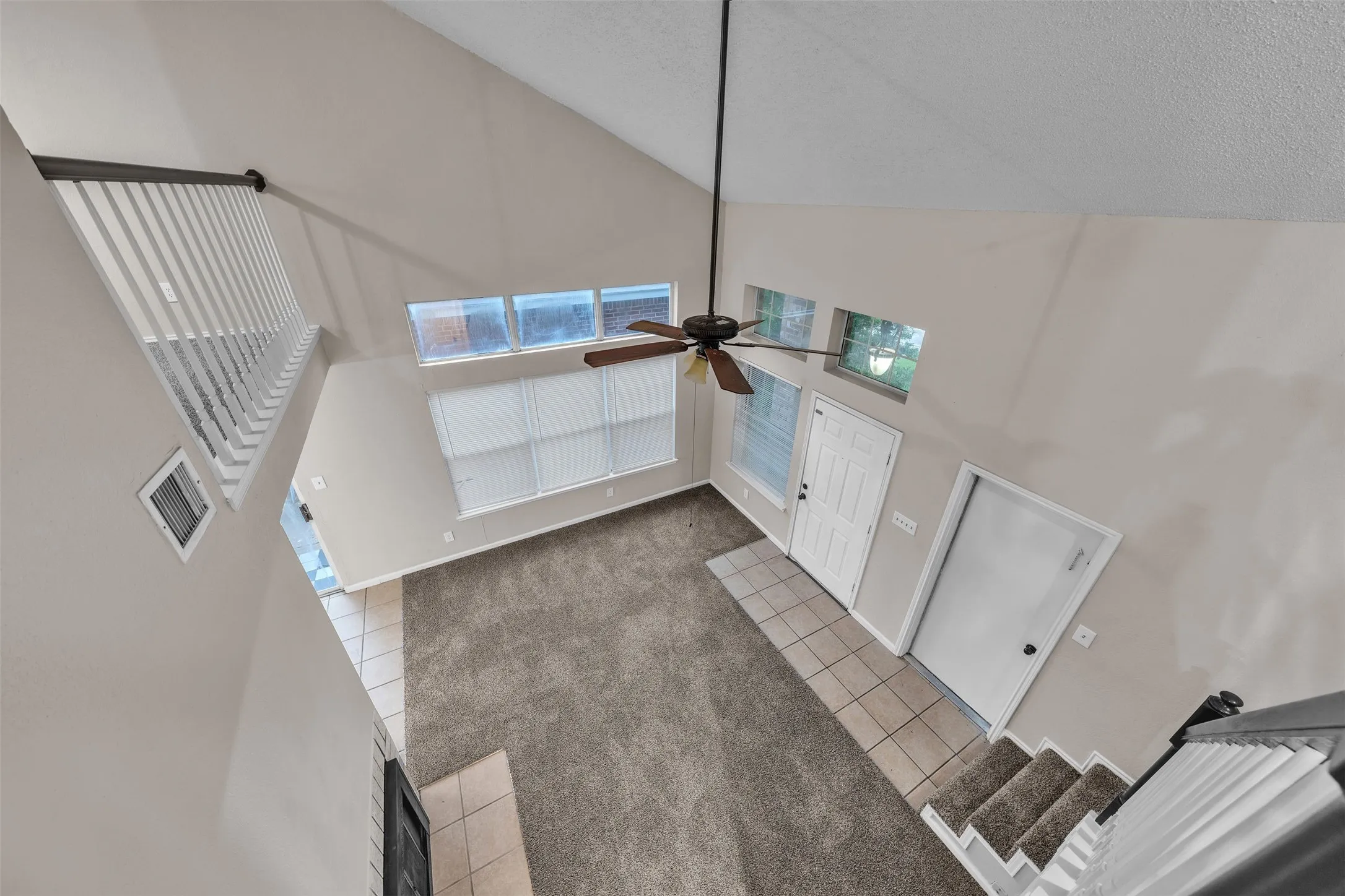 Vaulted ceiling living area featuring a ceiling fan, carpet flooring, and tile entryway