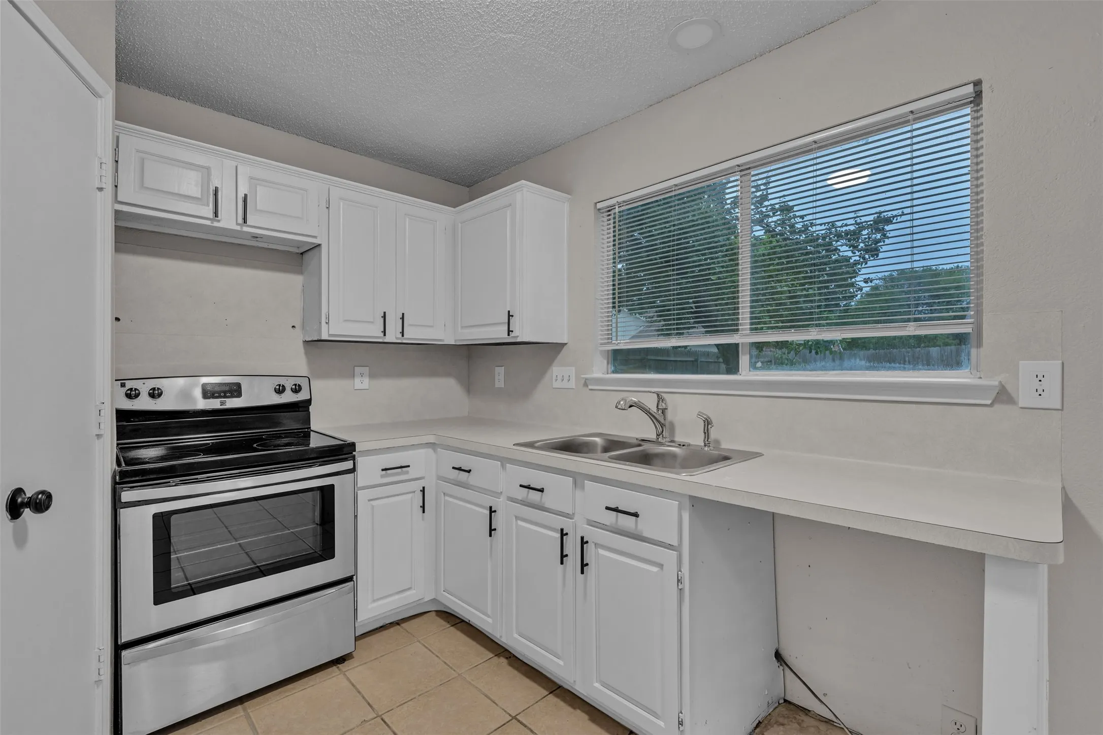 Kitchen featuring white cabinetry with black hardware, a stainless steel electric range, and a double basin sink
