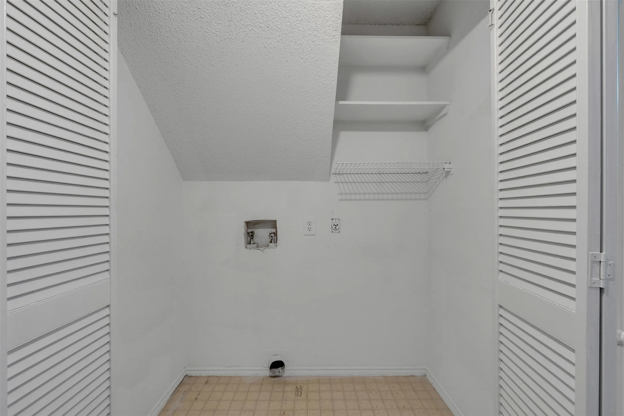 Utility closet featuring louvered bi-fold doors, white shelving, a wire storage rack, and hookups for appliances