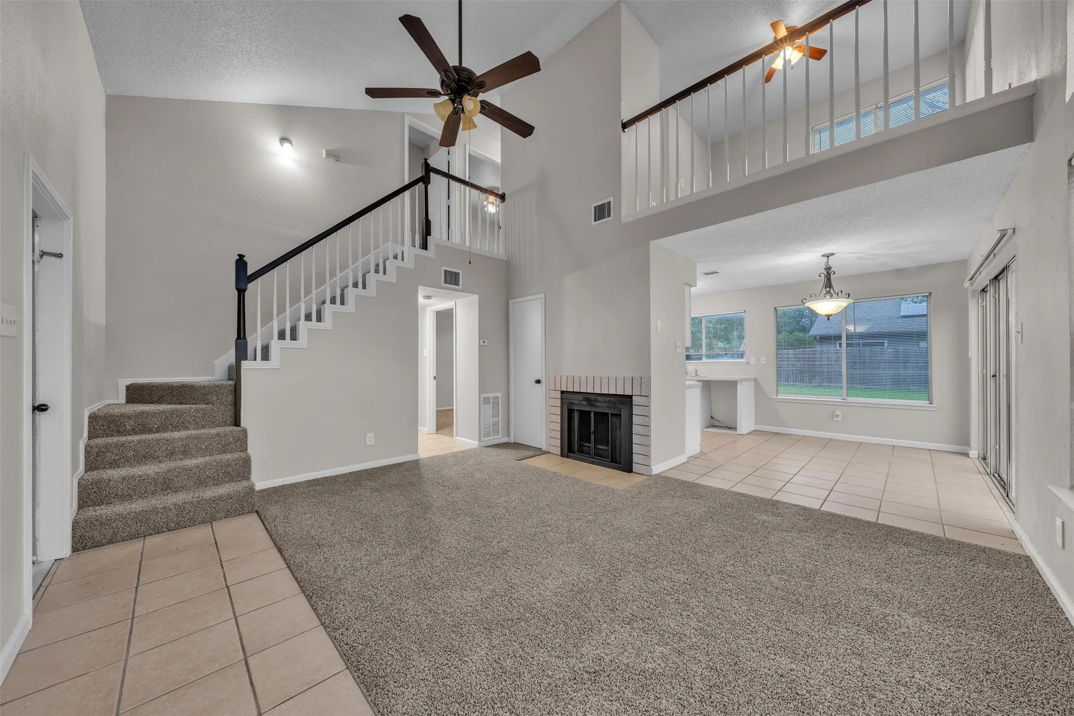 Vaulted living area featuring a fireplace with a brick surround, carpet flooring, a ceiling fan, and a view of the second-story loft