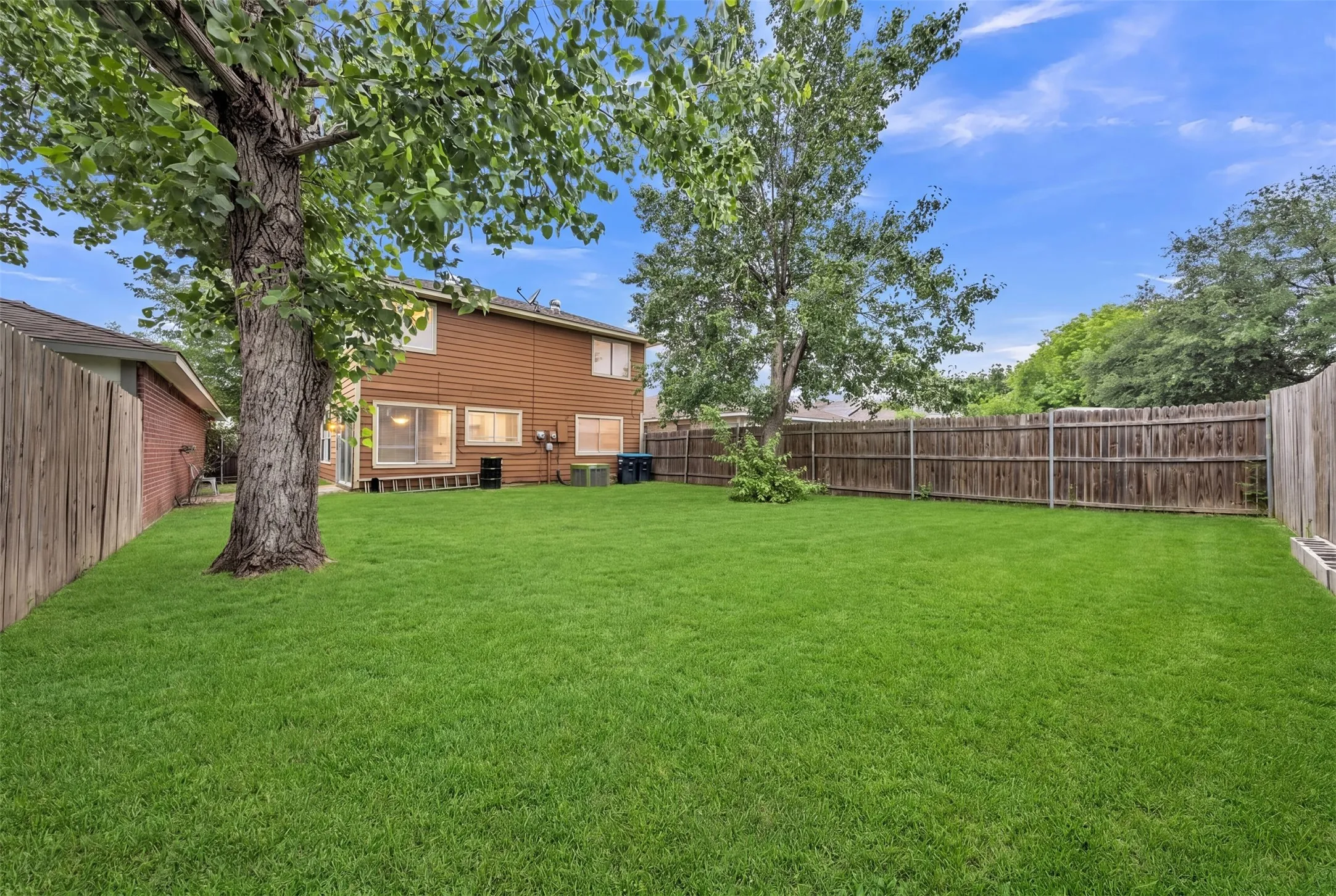 Expansive backyard featuring a large green lawn, mature trees, and a full privacy fence