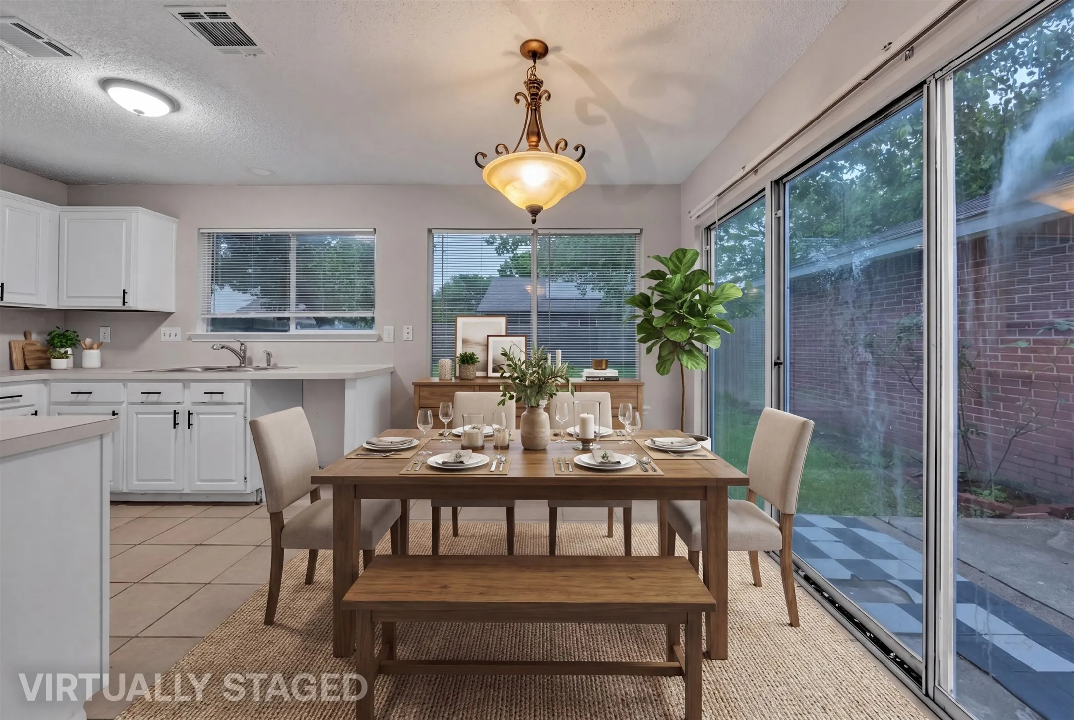 Open-concept dining area featuring a decorative chandelier, tile flooring, white cabinetry, and glass sliding doors providing access to the outdoors