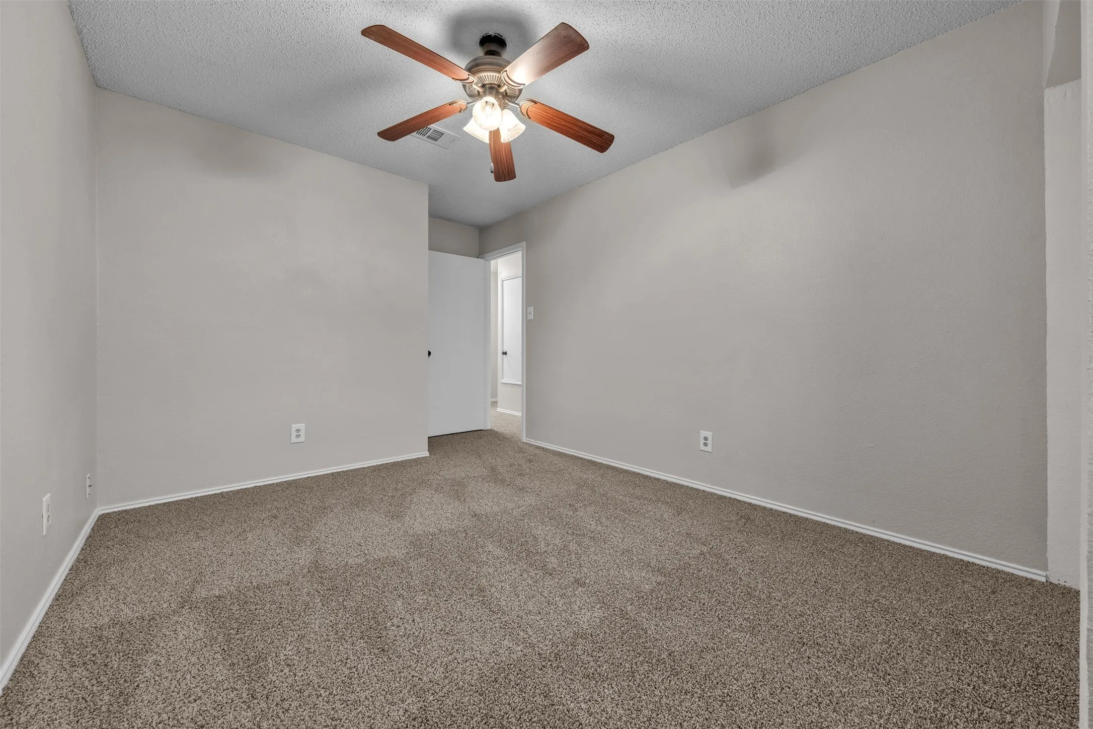Spacious room featuring neutral wall tones, textured ceiling, brown carpet, and a ceiling fan with light fixture