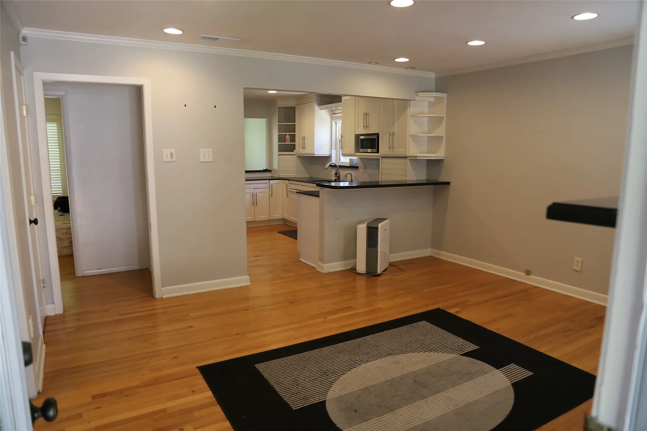 Open-concept living area featuring wood-finish flooring, recessed lighting, crown molding, a built-in breakfast bar, and kitchen cabinetry with integrated appliances