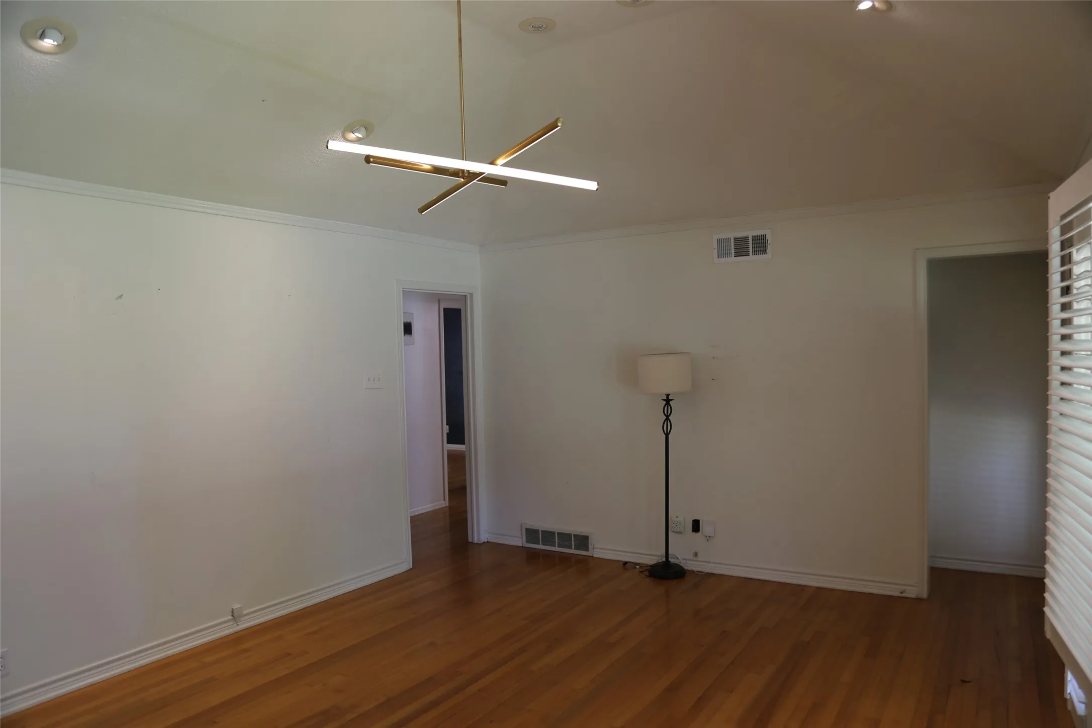 Spacious interior room featuring wood-finish flooring, white walls, and crown molding