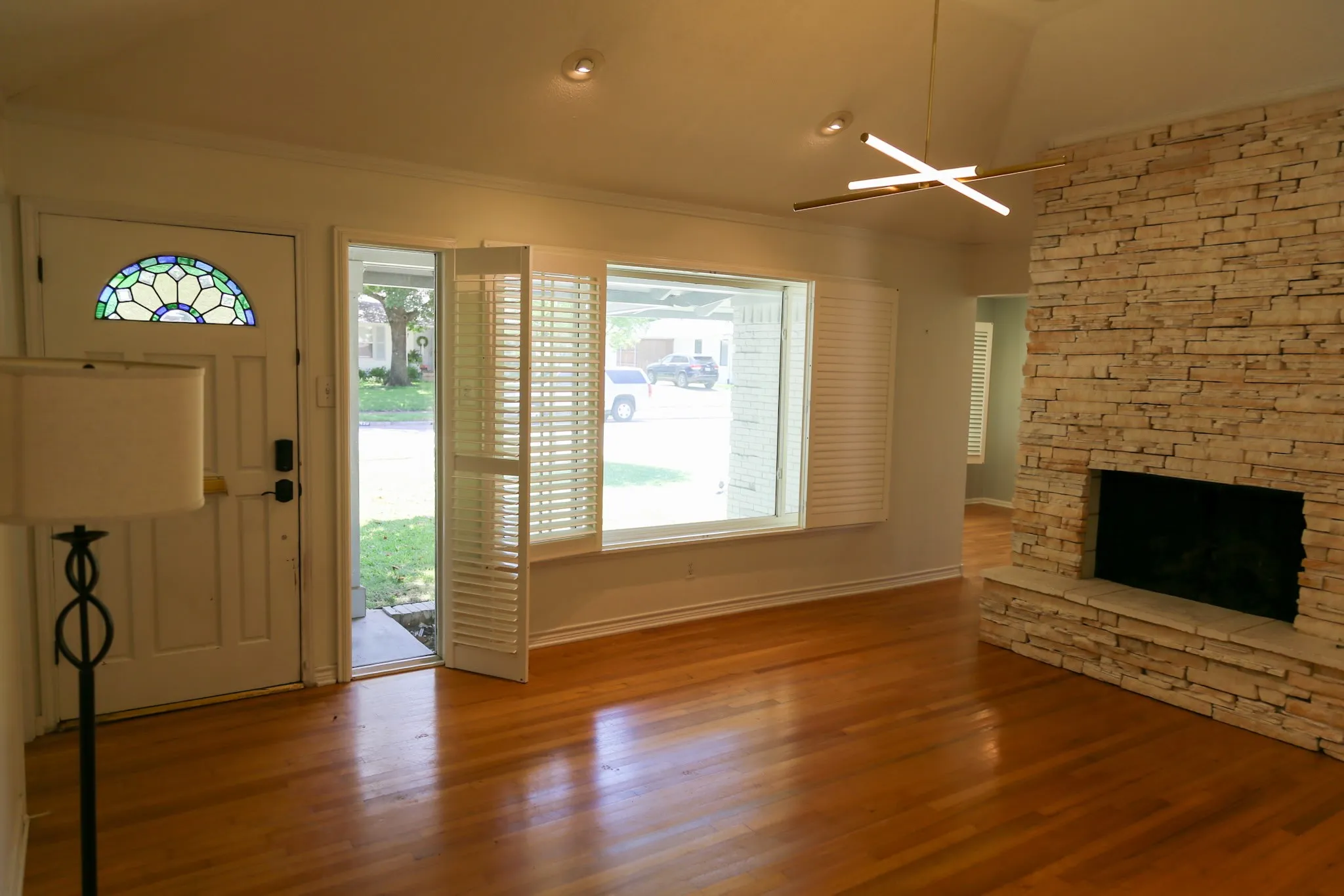 Living area featuring wood-finish flooring, a stone-clad fireplace, and a contemporary linear chandelier