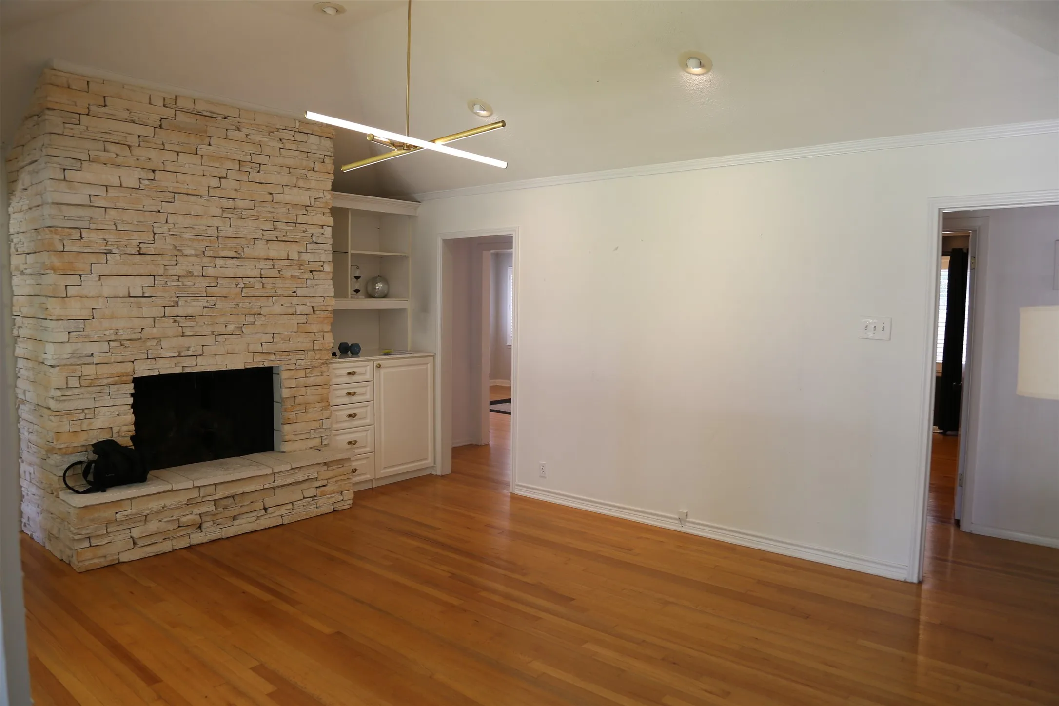 Stone fireplace with hearth and integrated built-in shelving, hardwood flooring, recessed lighting, and a modern linear light fixture
