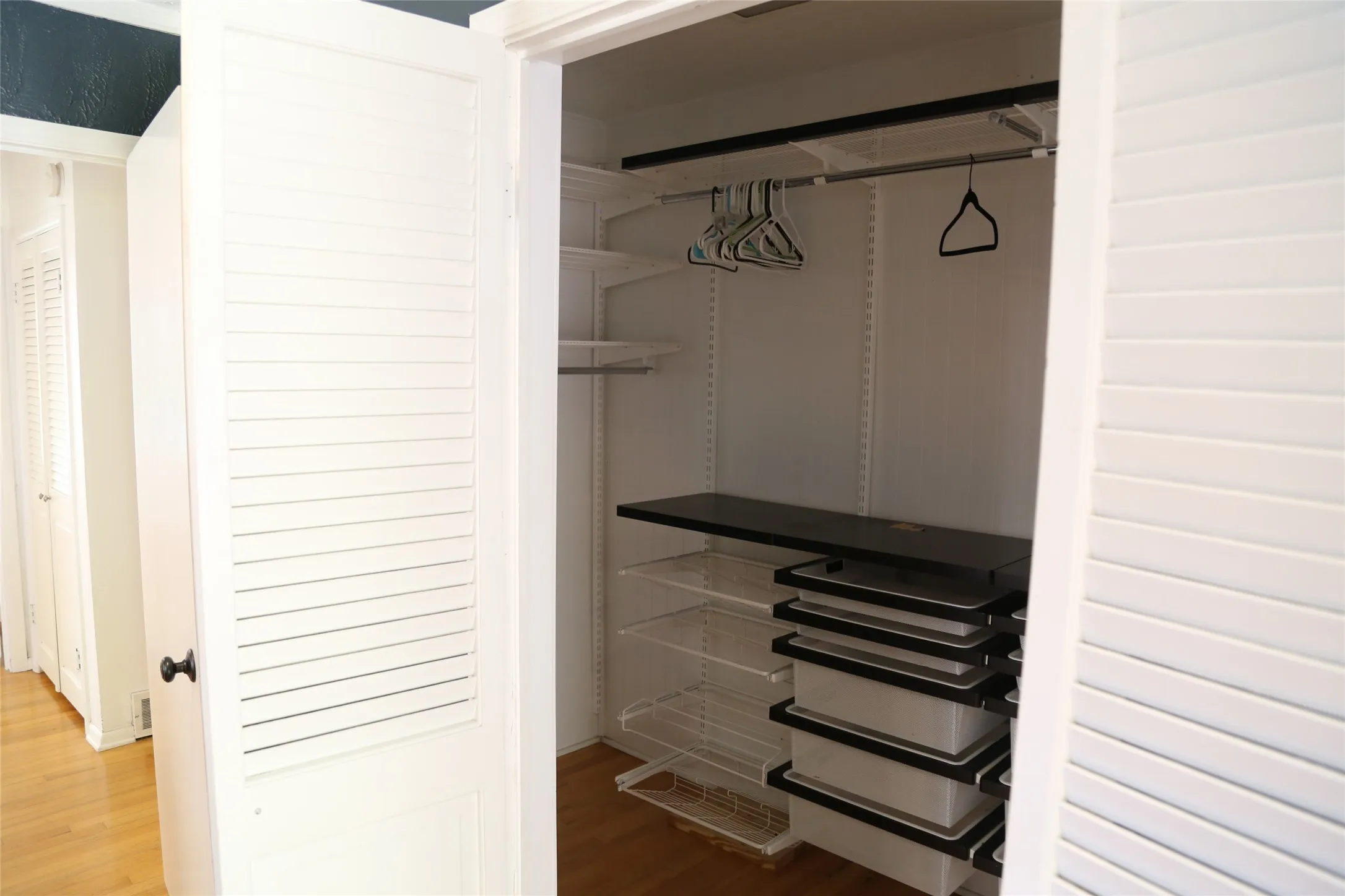 Louvered bifold doors open to an organized closet system featuring adjustable shelving, hanging rods, and pull-out storage bins