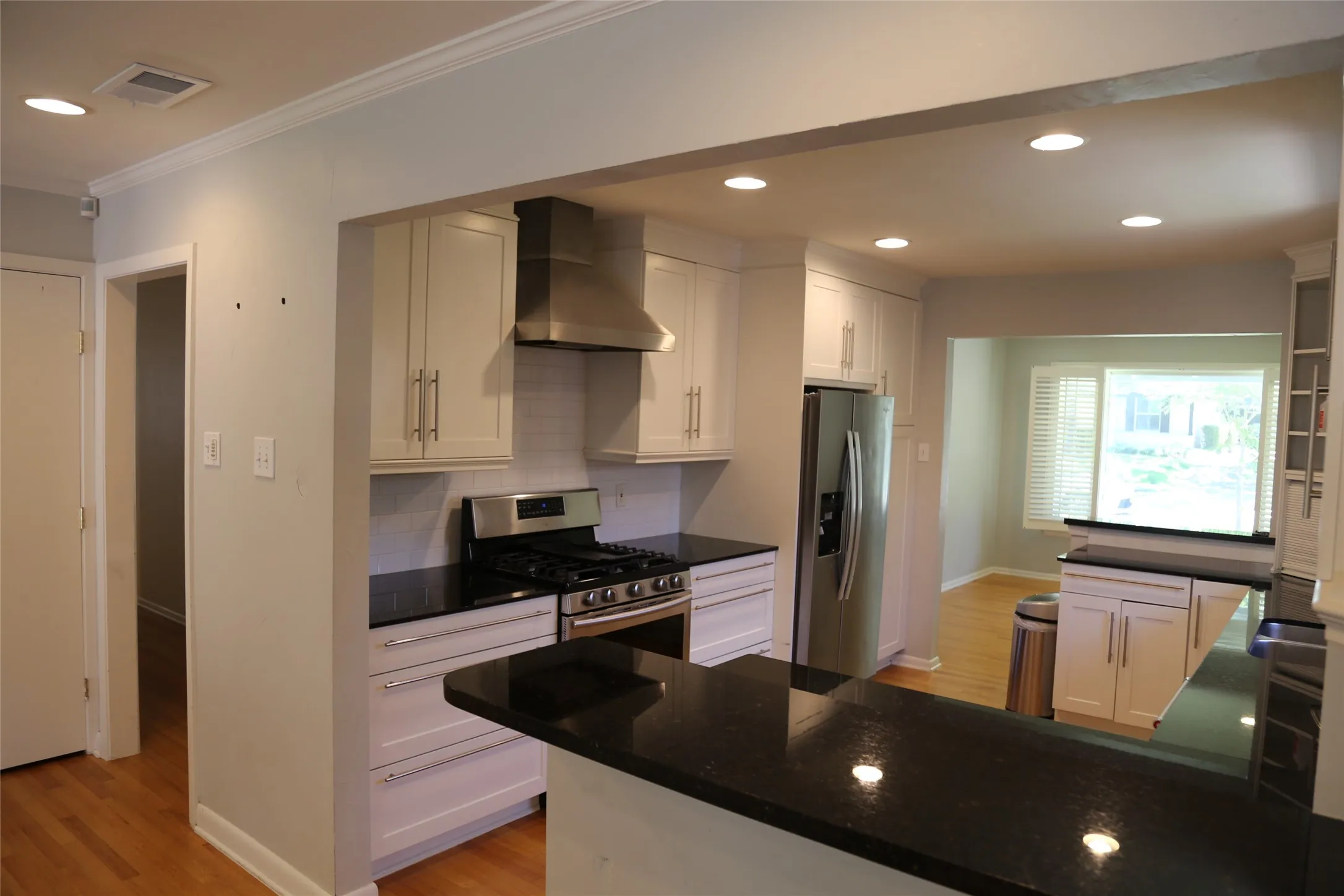 Kitchen featuring white cabinetry, black countertops, stainless steel appliances, and wood-finish flooring