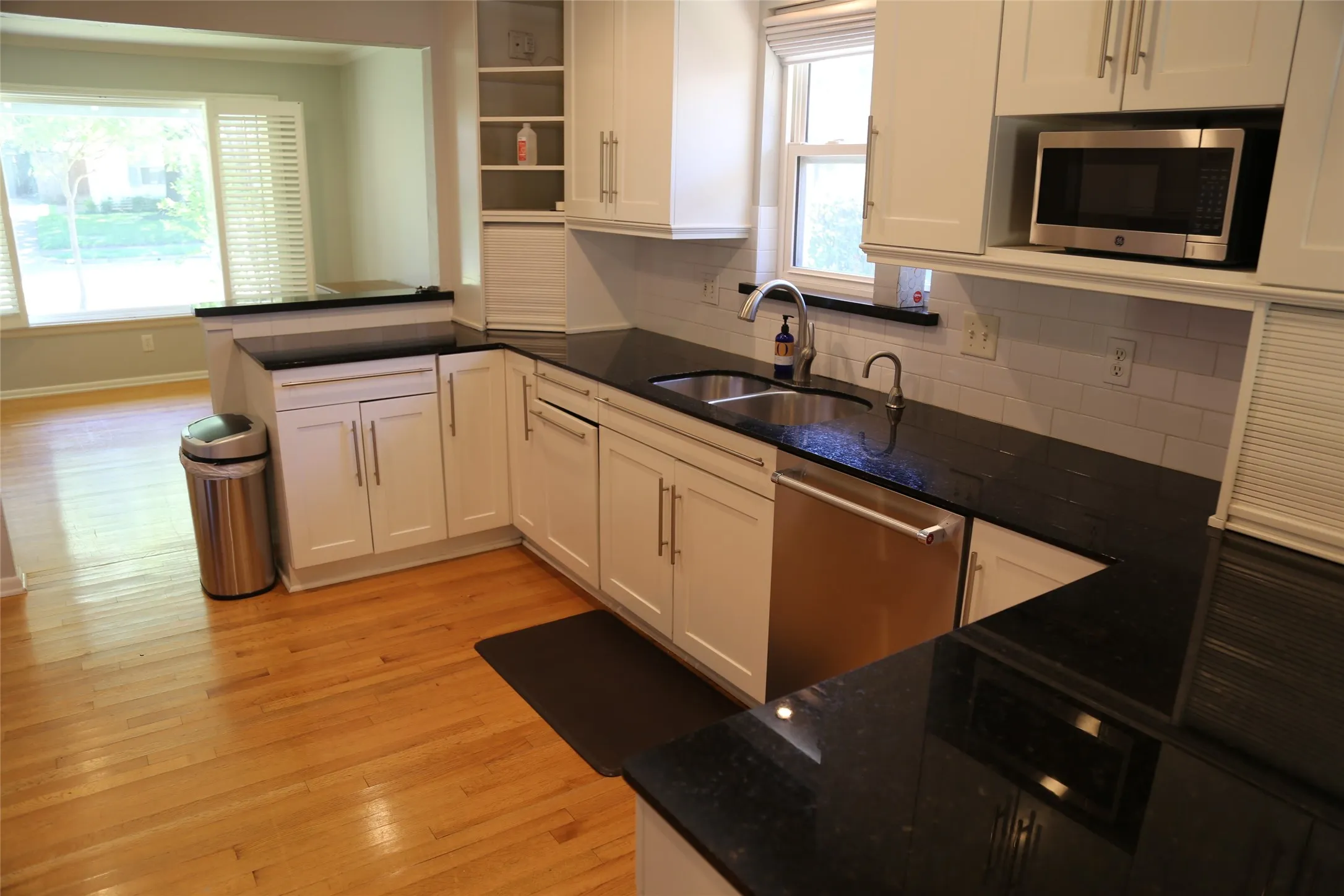 Kitchen featuring white cabinetry, dark countertops, a stainless steel sink with a gooseneck faucet, a built-in microwave, and wood-finish flooring