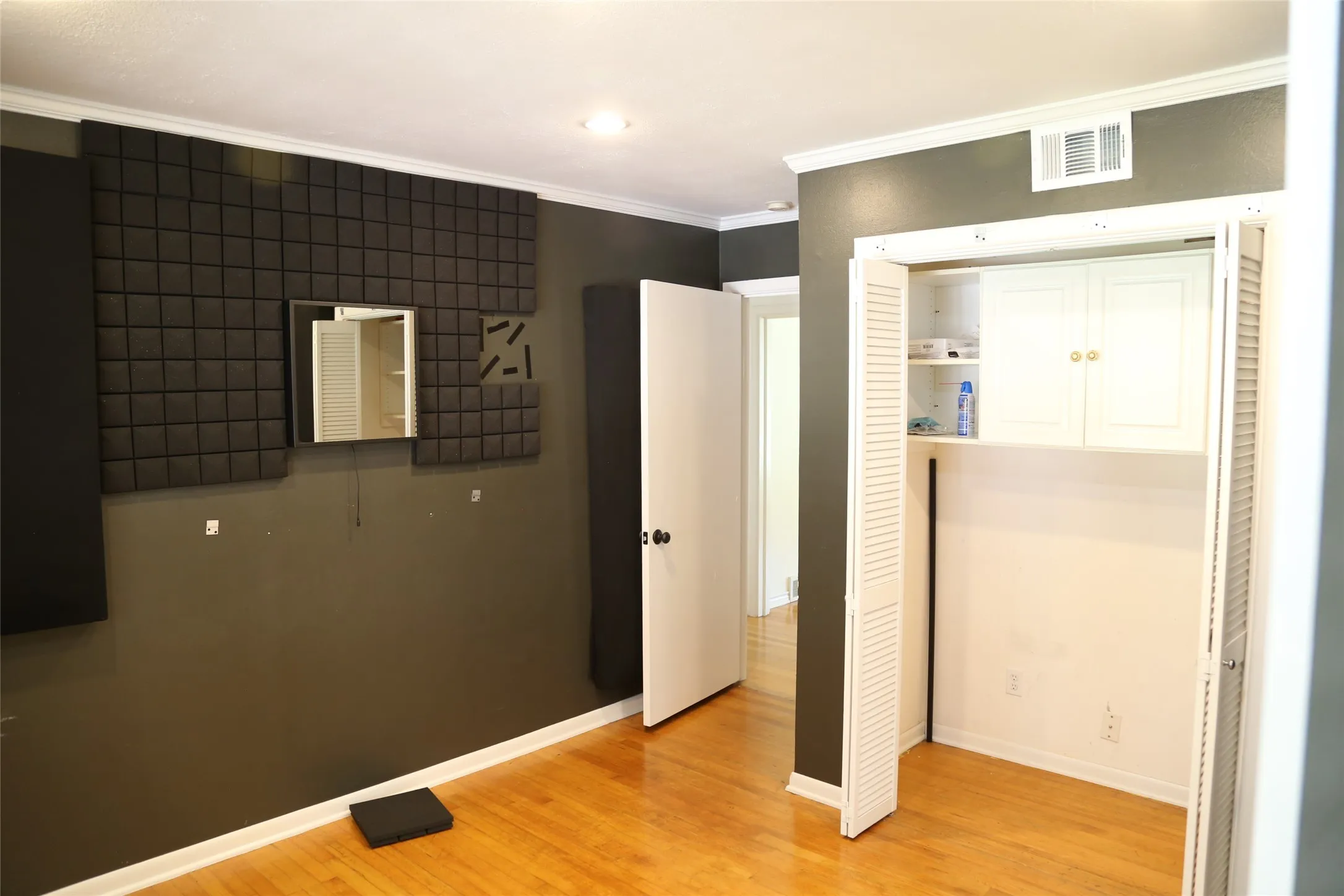 Room featuring wood-finish flooring, crown molding, and a built-in closet with louvered bi-fold doors and upper cabinetry