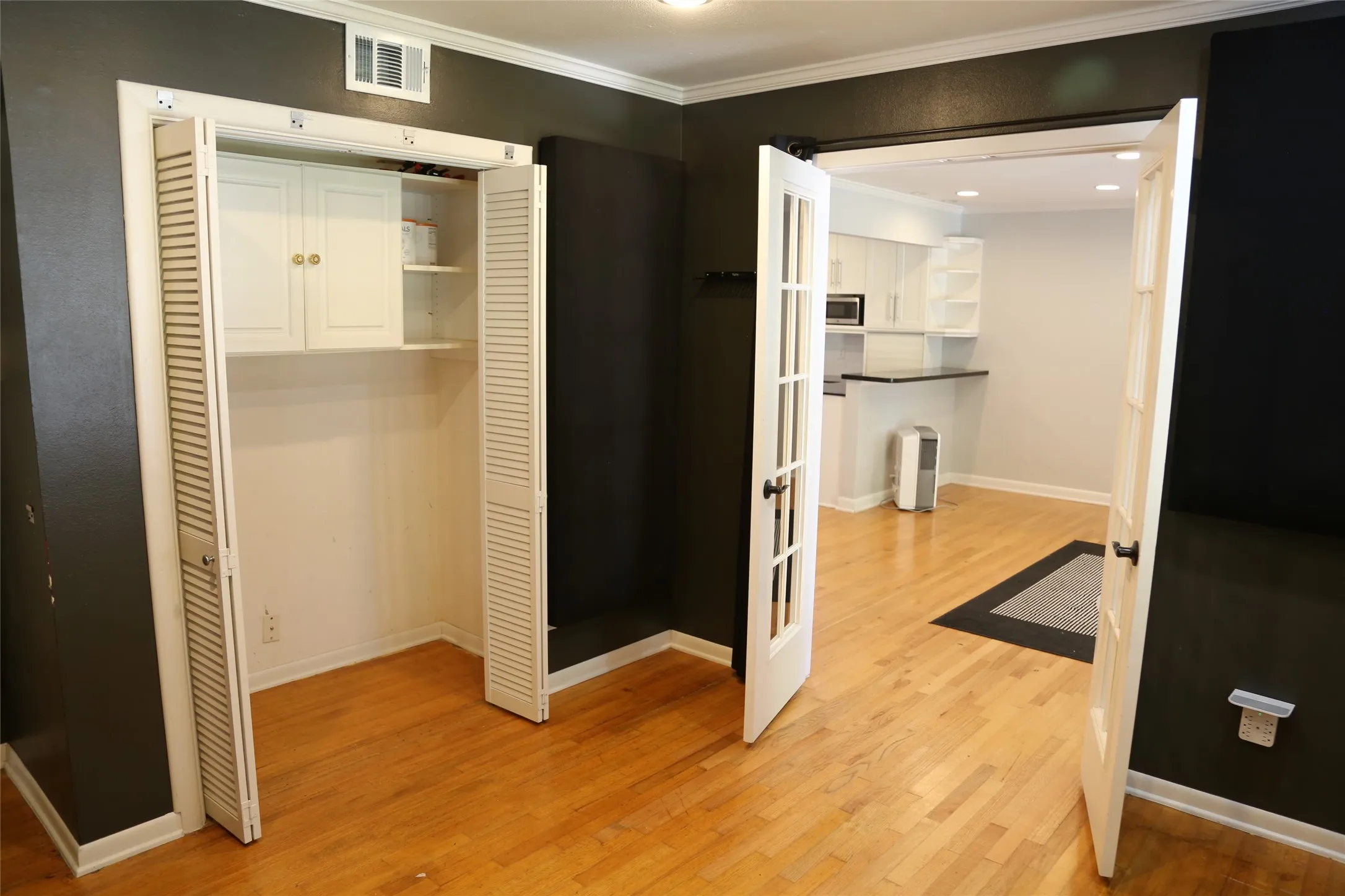 Hardwood flooring throughout featuring French doors opening to a kitchen space with white cabinetry, black countertops, and a built-in microwave