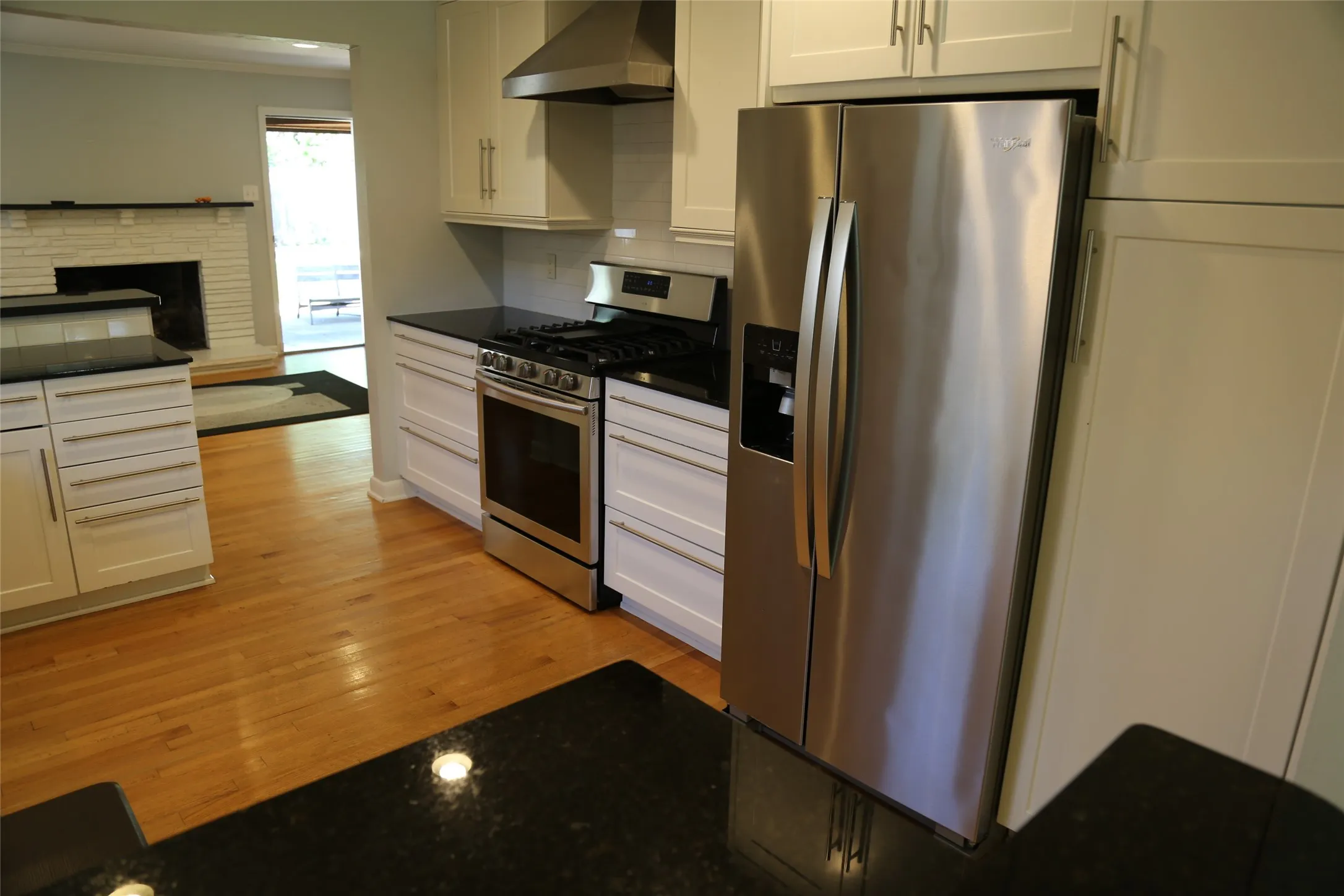 Kitchen featuring wood-finish flooring, stainless steel appliances, black countertops, white shaker-style cabinetry, and a white subway tile backsplash