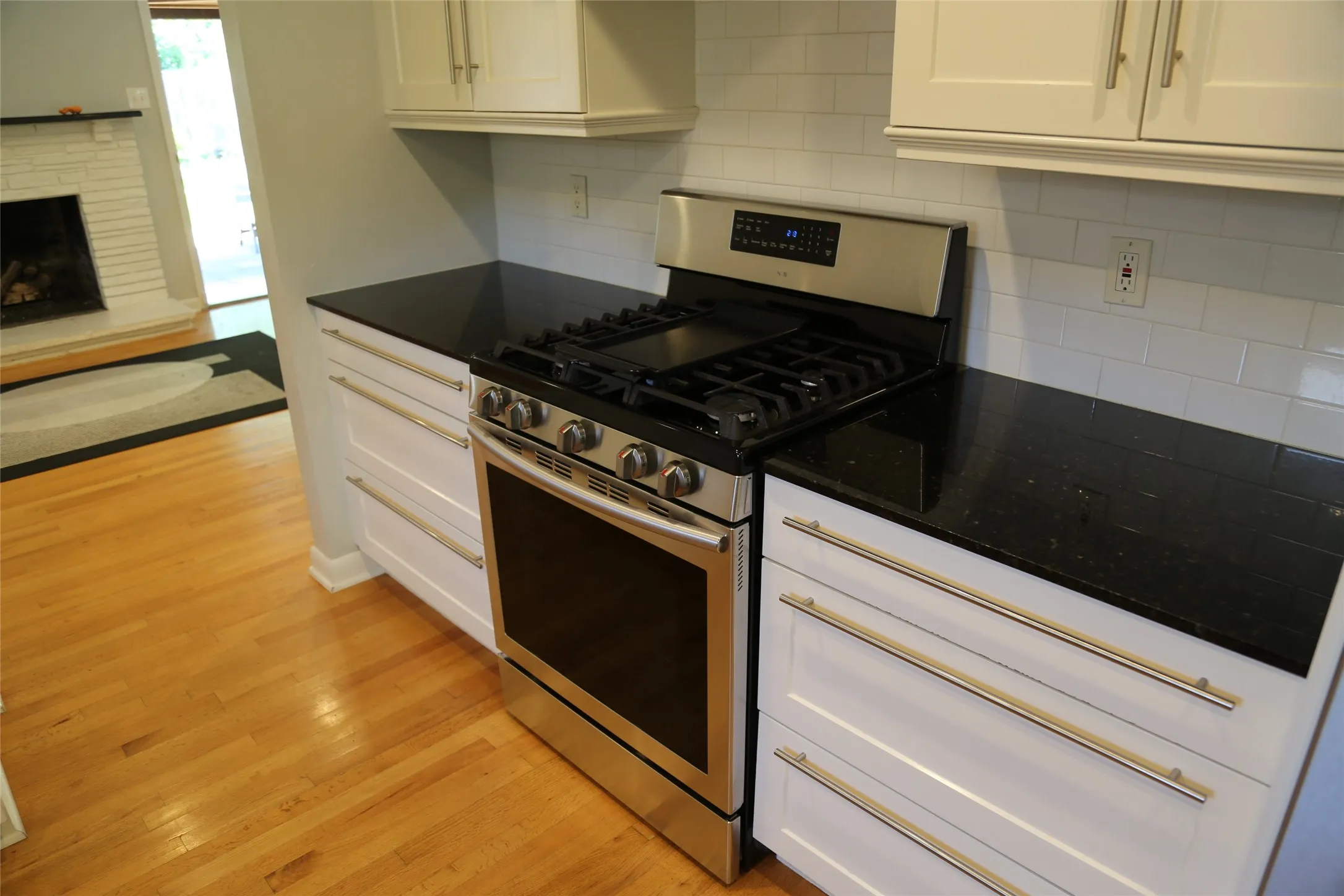 Kitchen featuring a stainless steel range, dark countertops, white subway tile backsplash, white cabinetry with contemporary hardware, and wood-finish flooring
