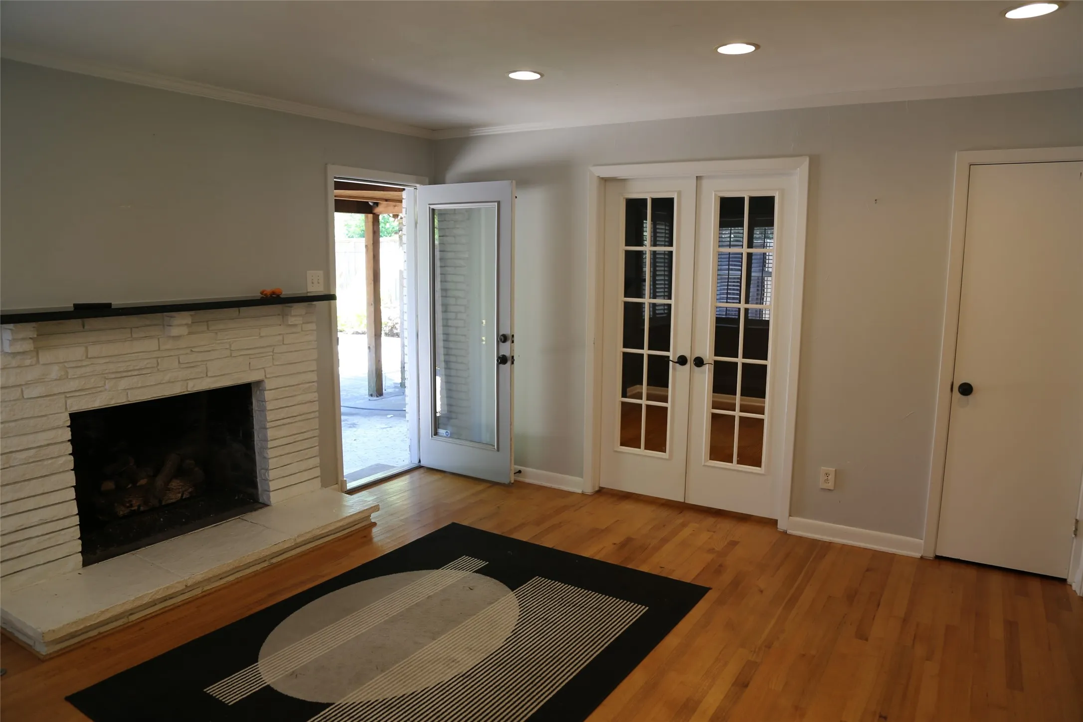 Living area featuring a white brick fireplace with a dark mantel, wood-finish flooring, recessed lighting, and white French doors