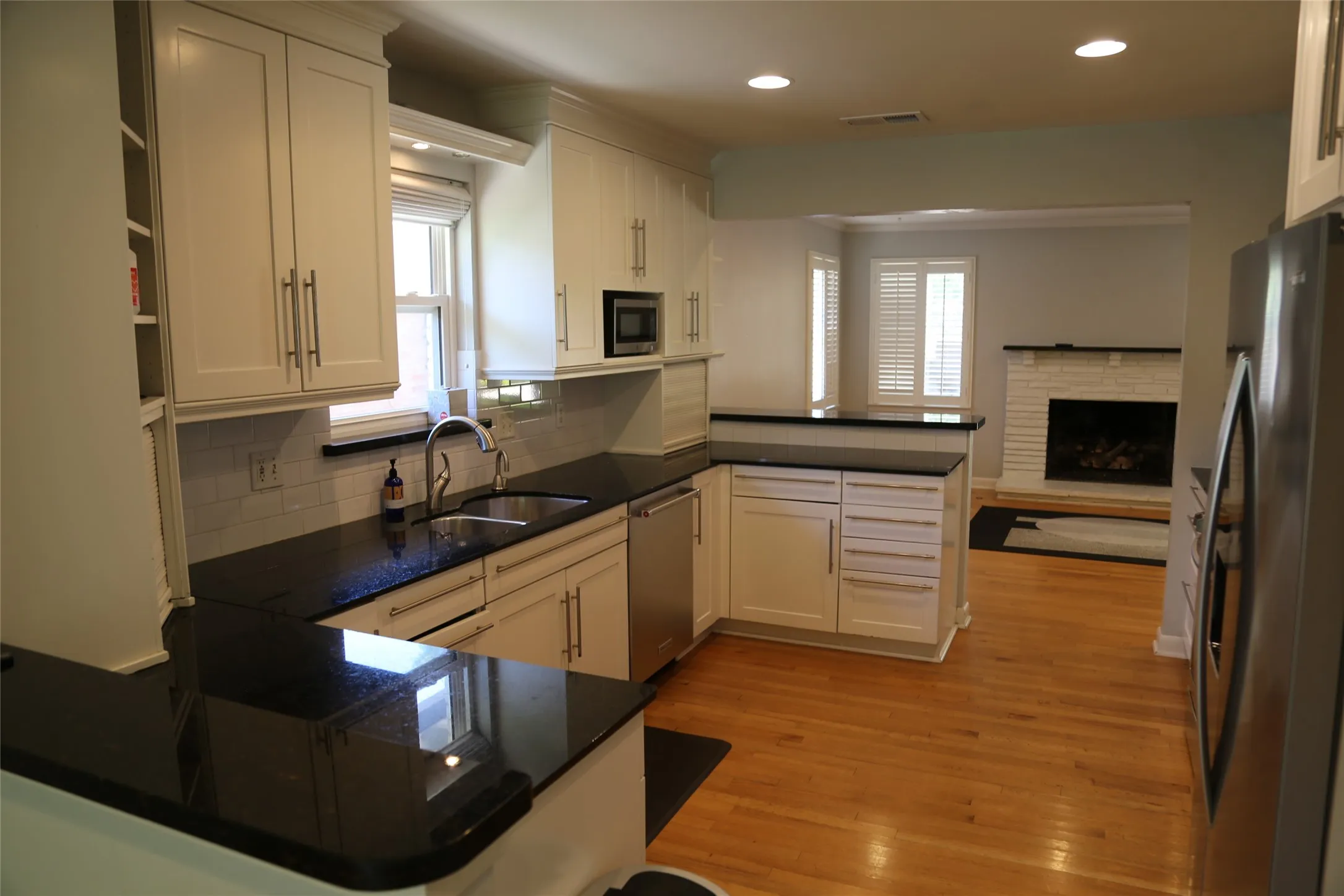 Bright kitchen featuring white cabinetry, dark countertops, a stainless steel sink, and wood-finish flooring