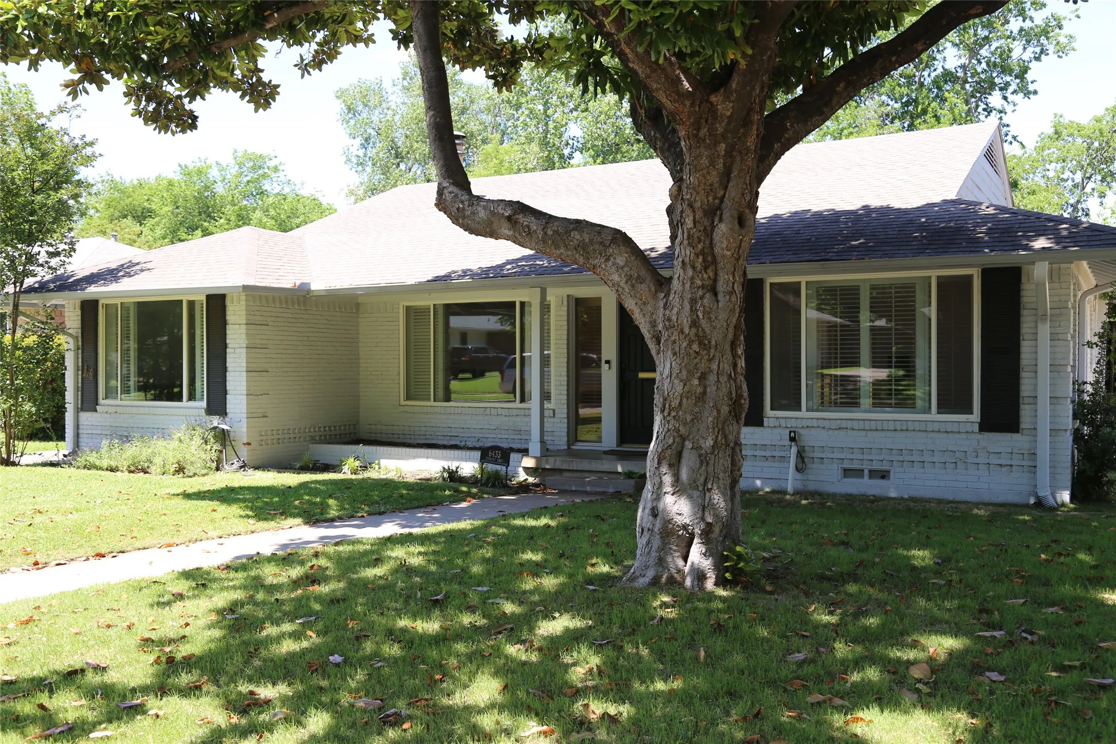Front exterior featuring painted brick siding, a light-colored roof, dark shutters, and a concrete walkway