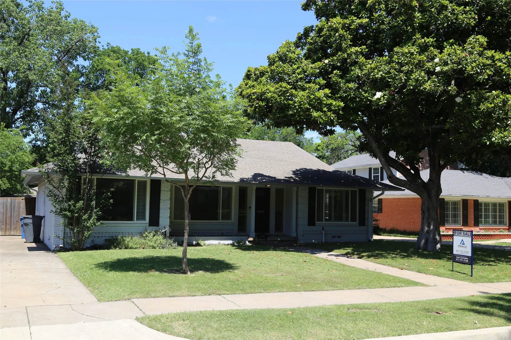 Single-story residence featuring a gray exterior siding, a dark shingle roof, and a mature shade tree