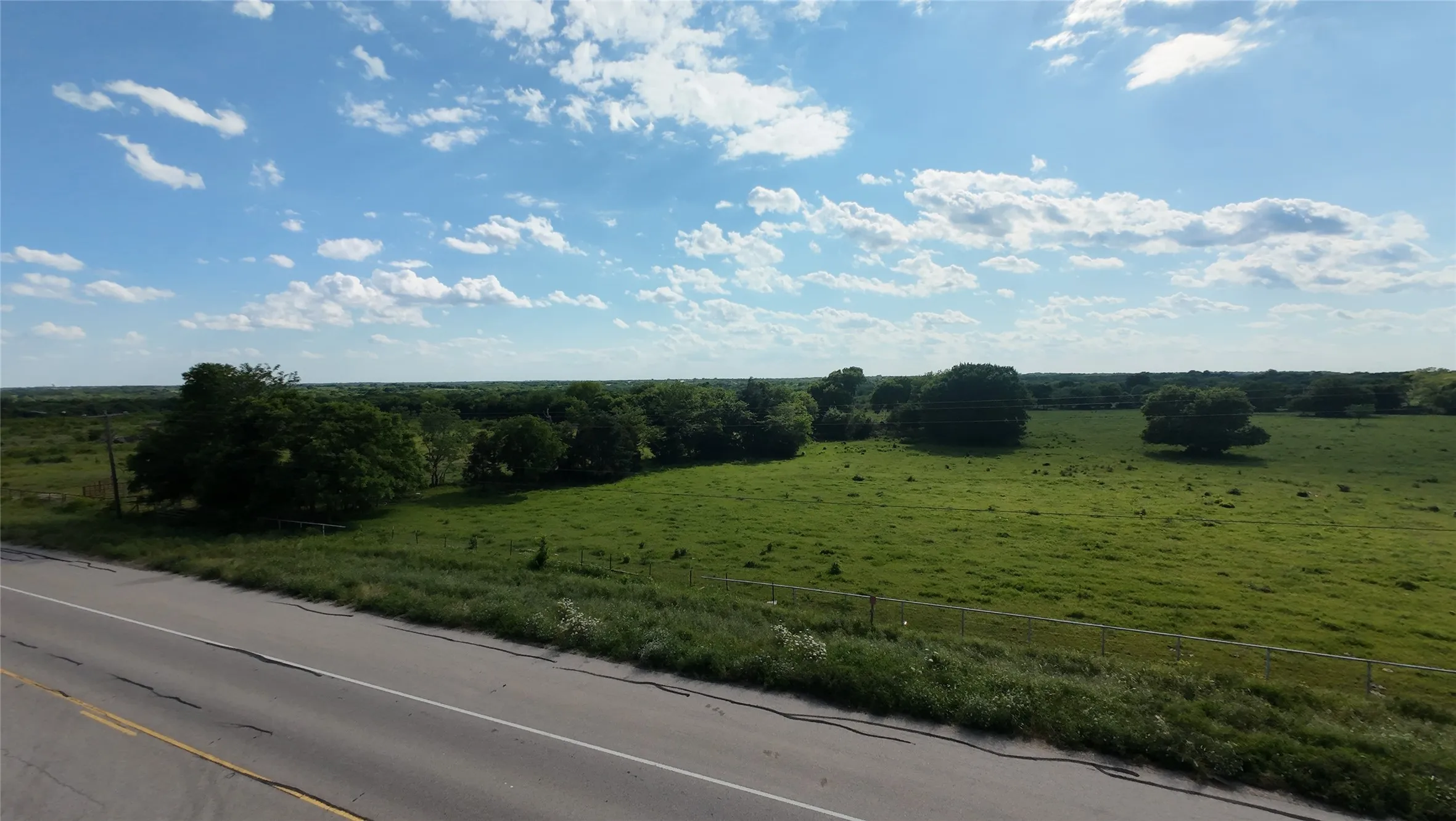 Expansive green pasture with scattered mature trees and a distant tree line