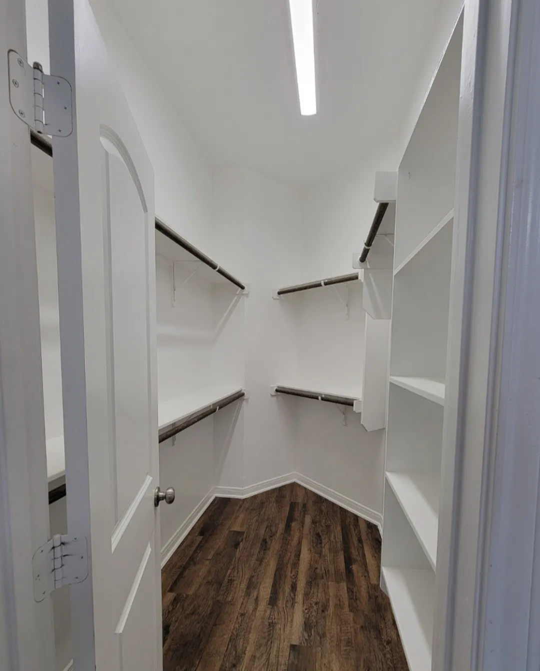 Spacious walk-in closet featuring white built-in shelving, hanging rods, and wood-finish flooring