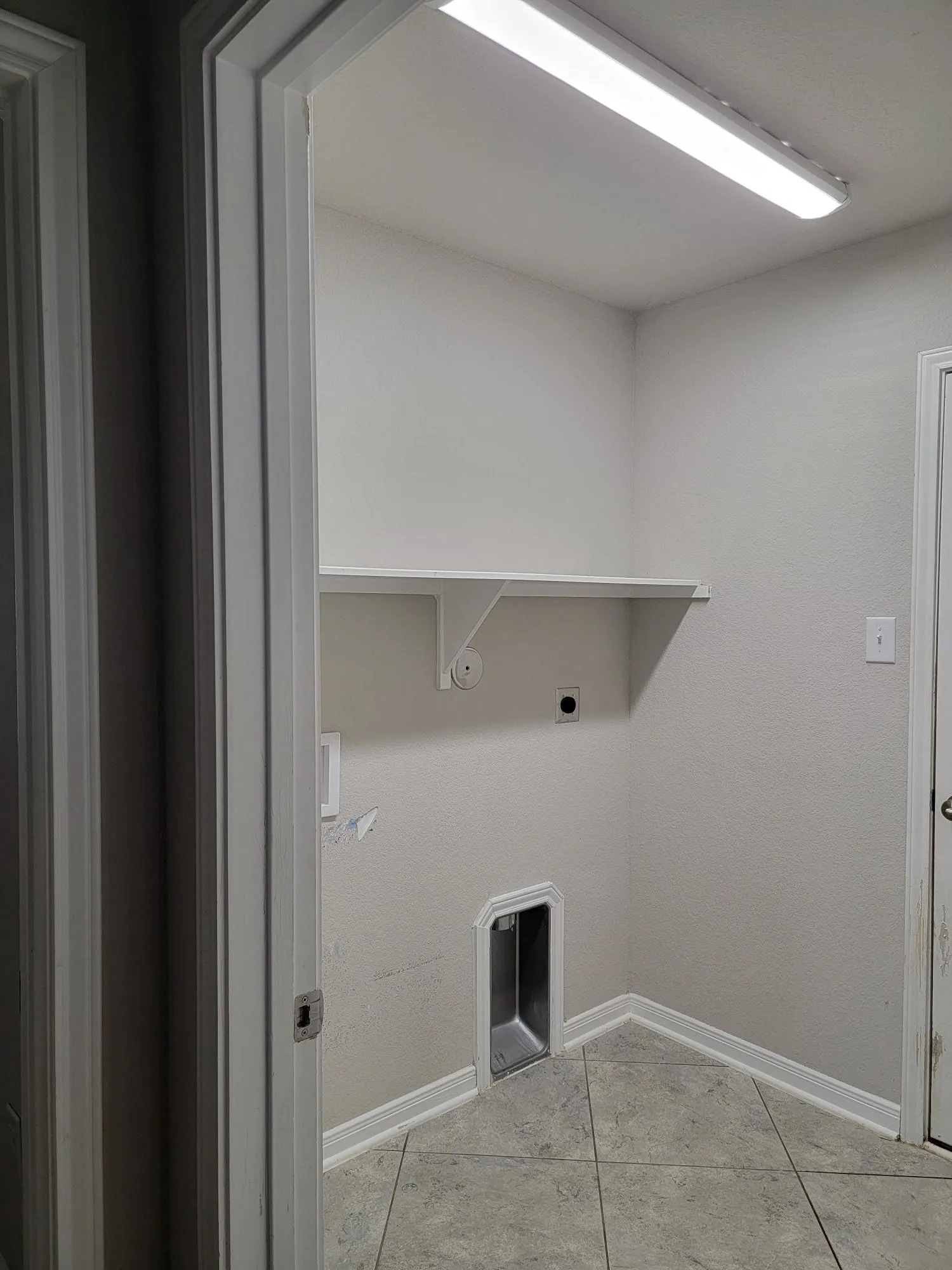Dedicated laundry area featuring ceramic tile flooring, a built-in shelf, and a ceiling-mounted fluorescent light fixture