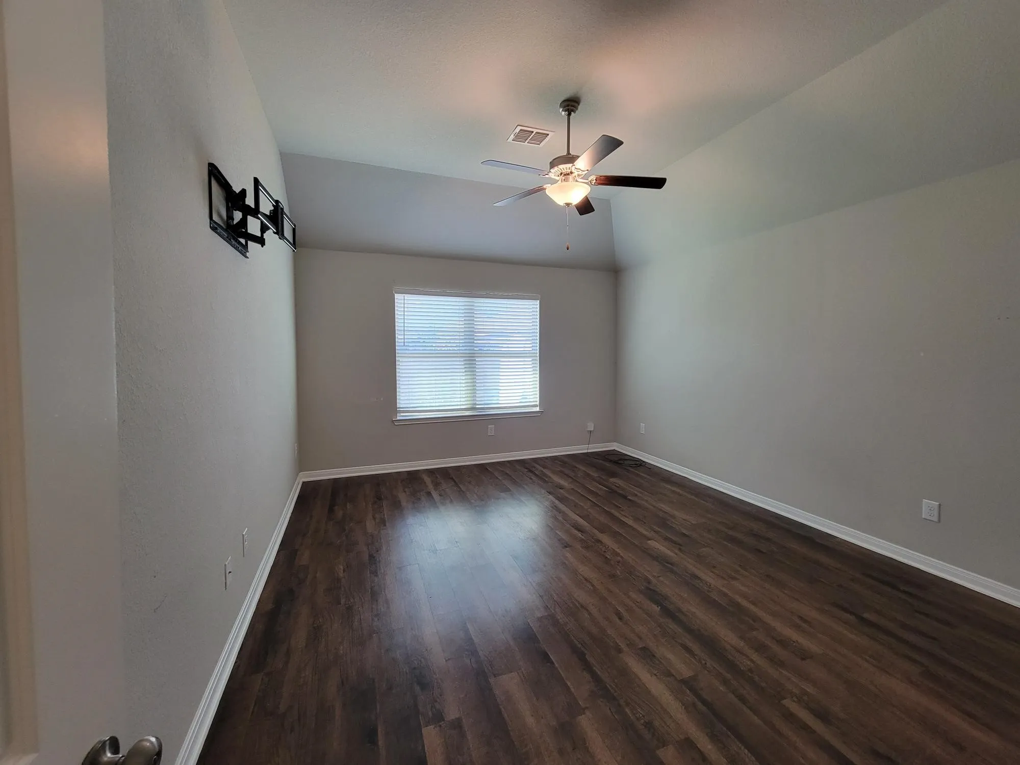 Spacious room featuring vaulted ceilings, a ceiling fan with integrated lighting, wood-finish flooring, and a window with horizontal blinds