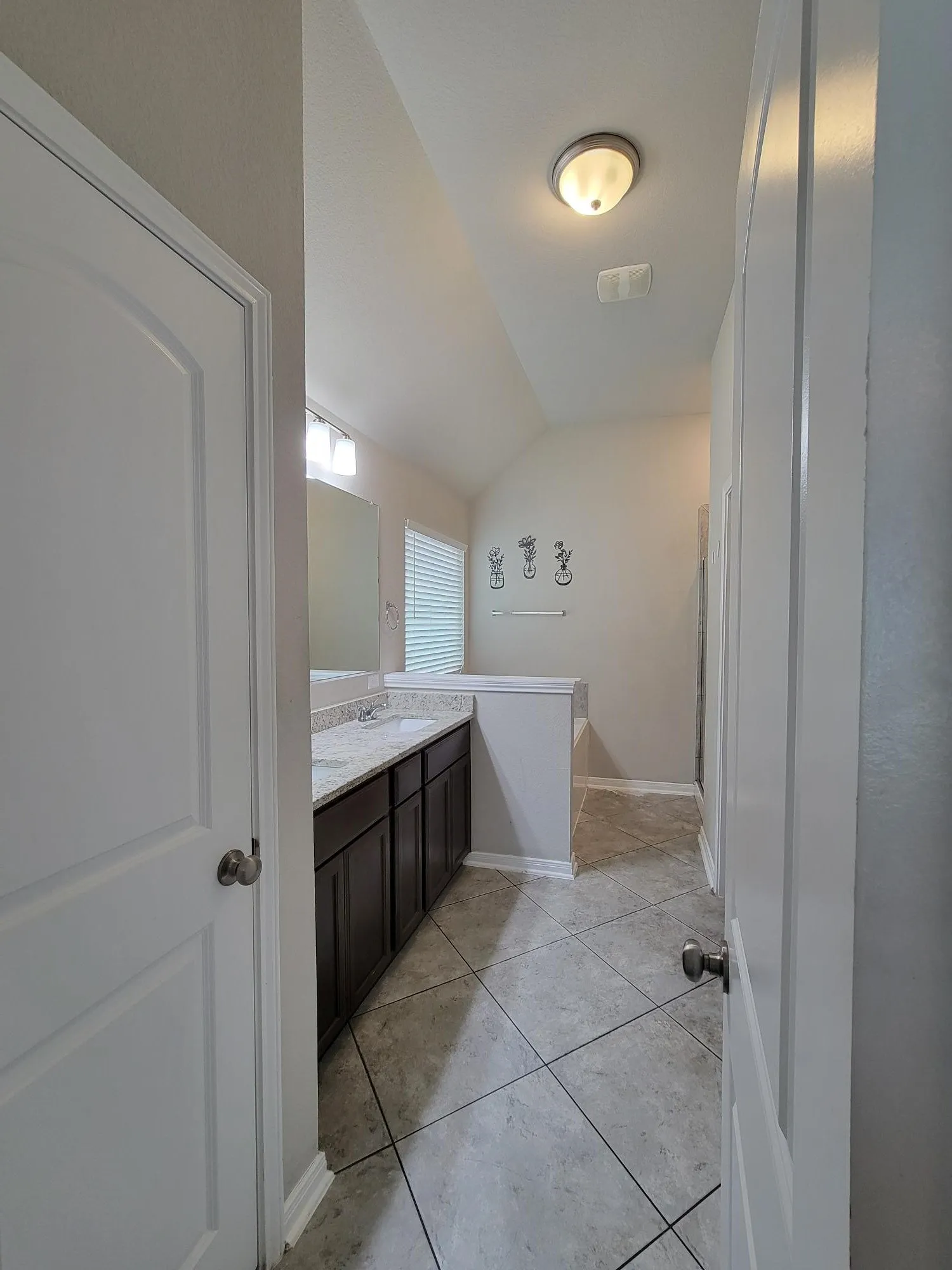 Spacious bathroom with dual vanities, stone-finish countertops, dark wood cabinetry, and neutral-toned tile flooring