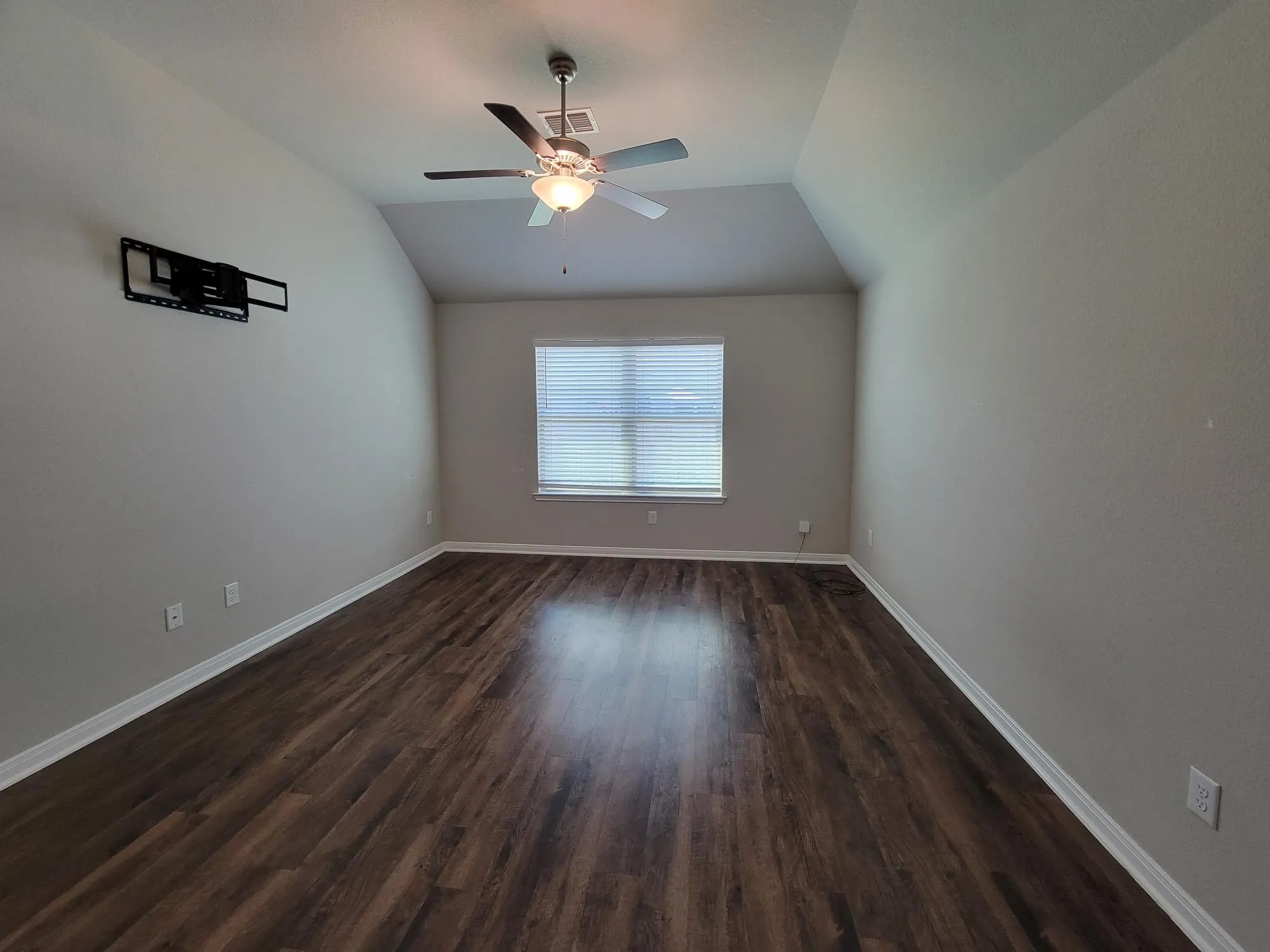 Spacious interior room featuring wood-finish flooring, a vaulted ceiling, and a ceiling fan with integrated lighting