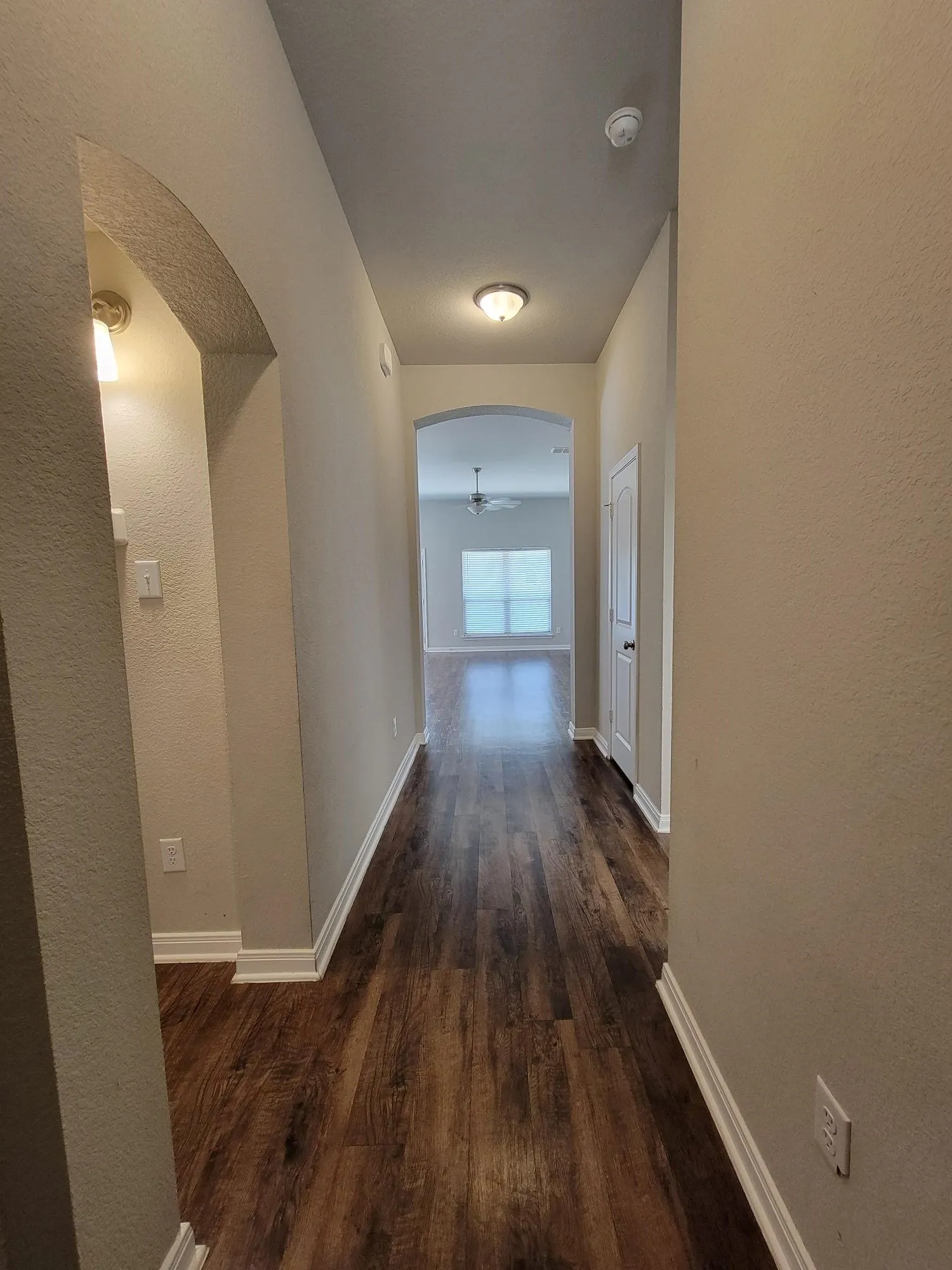 Hallway featuring wood-finish flooring, light neutral wall paint, and white baseboards