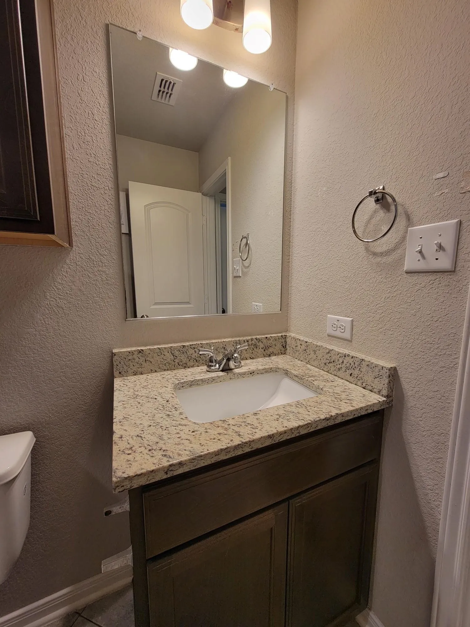 Bathroom vanity featuring a speckled countertop, undermount sink, and dark wood-finish cabinetry