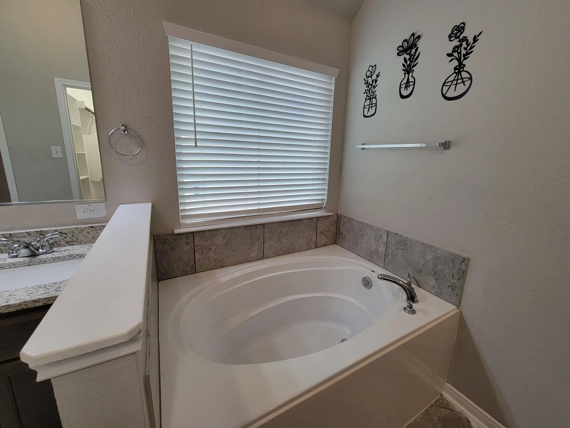 Garden tub with chrome fixtures, surrounded by gray tile wainscoting and a window with blinds