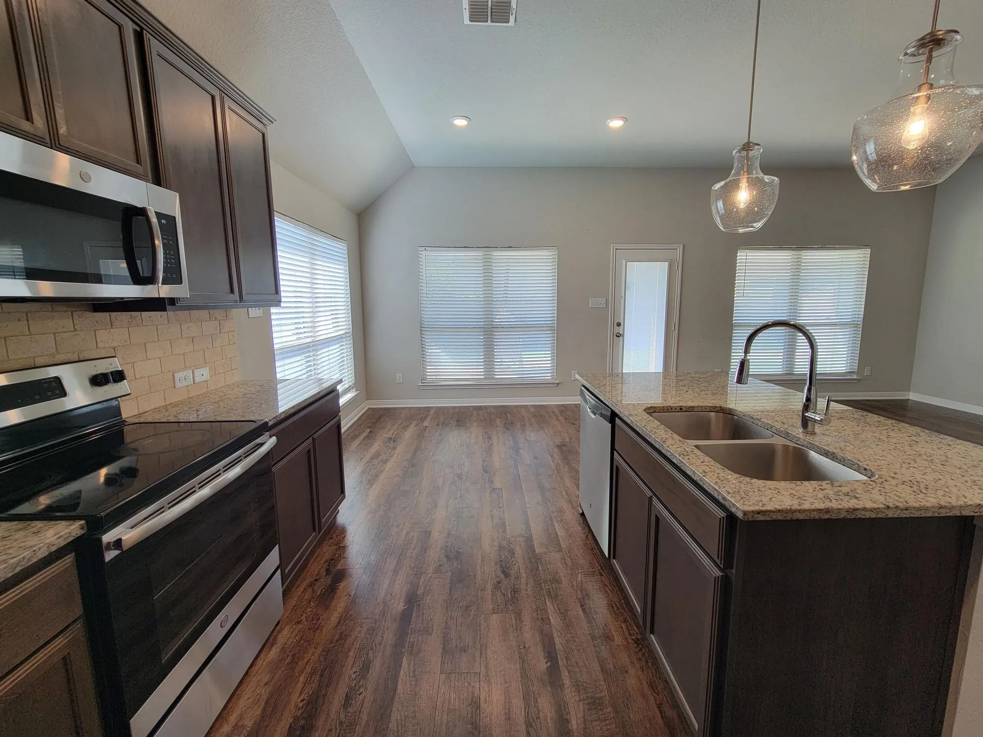 Kitchen featuring dark wood cabinetry, stainless steel appliances, speckled stone countertops, and a subway tile backsplash