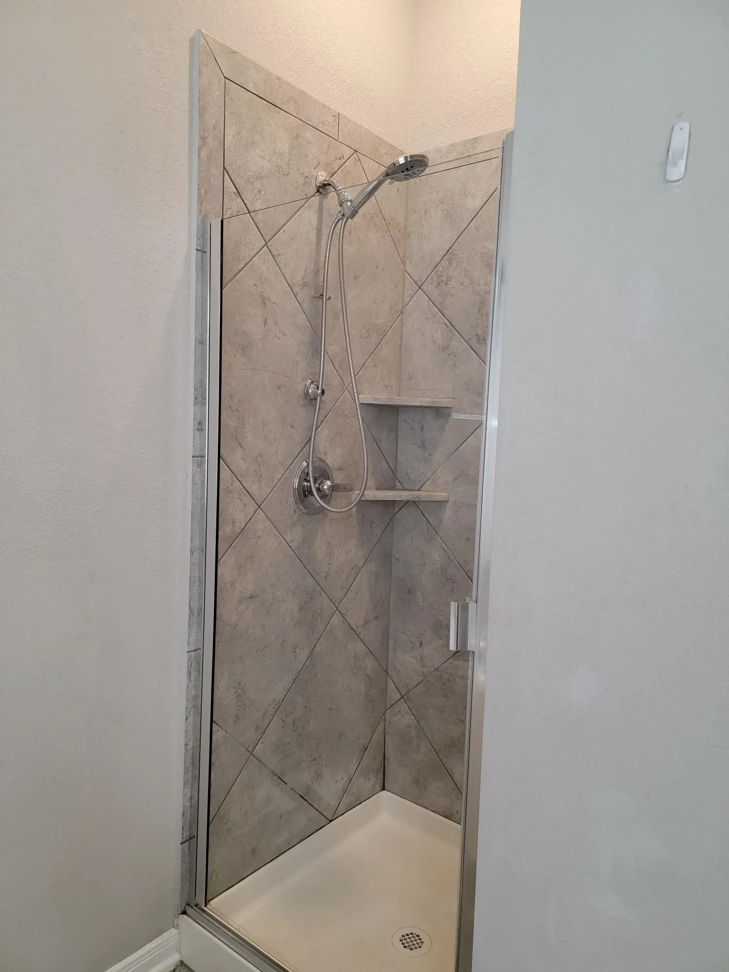Shower enclosure featuring a frameless glass door, diagonal tile surround, dual showerheads, and built-in shelving