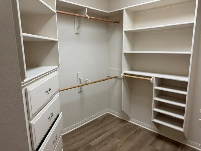 Built-in closet system featuring white cabinetry, multiple shelves, integrated drawers, and wood-finish flooring