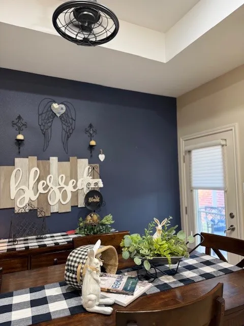 Dining area featuring a dark wood-finish table and chairs, a white trim door with privacy blinds, and a built-in ceiling fan with a black metal cage