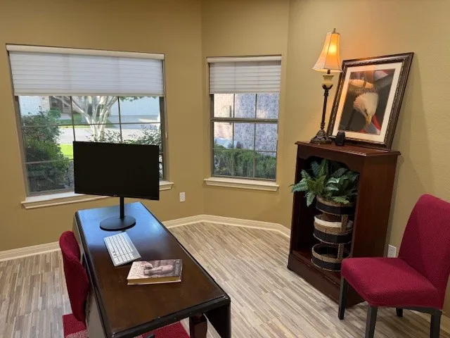 Versatile room featuring two windows with privacy blinds, light wood-finish flooring, and warm neutral wall tones