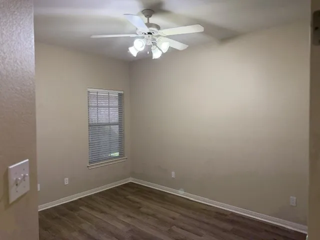 Wood-finish flooring, single window with blinds, ceiling fan with integrated lighting, and neutral wall tones