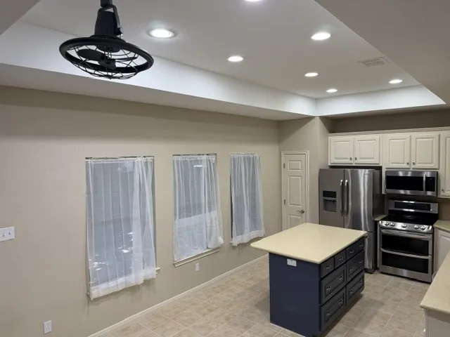 Kitchen featuring white upper cabinetry, a blue island with light-toned countertop, stainless steel appliances, and recessed lighting